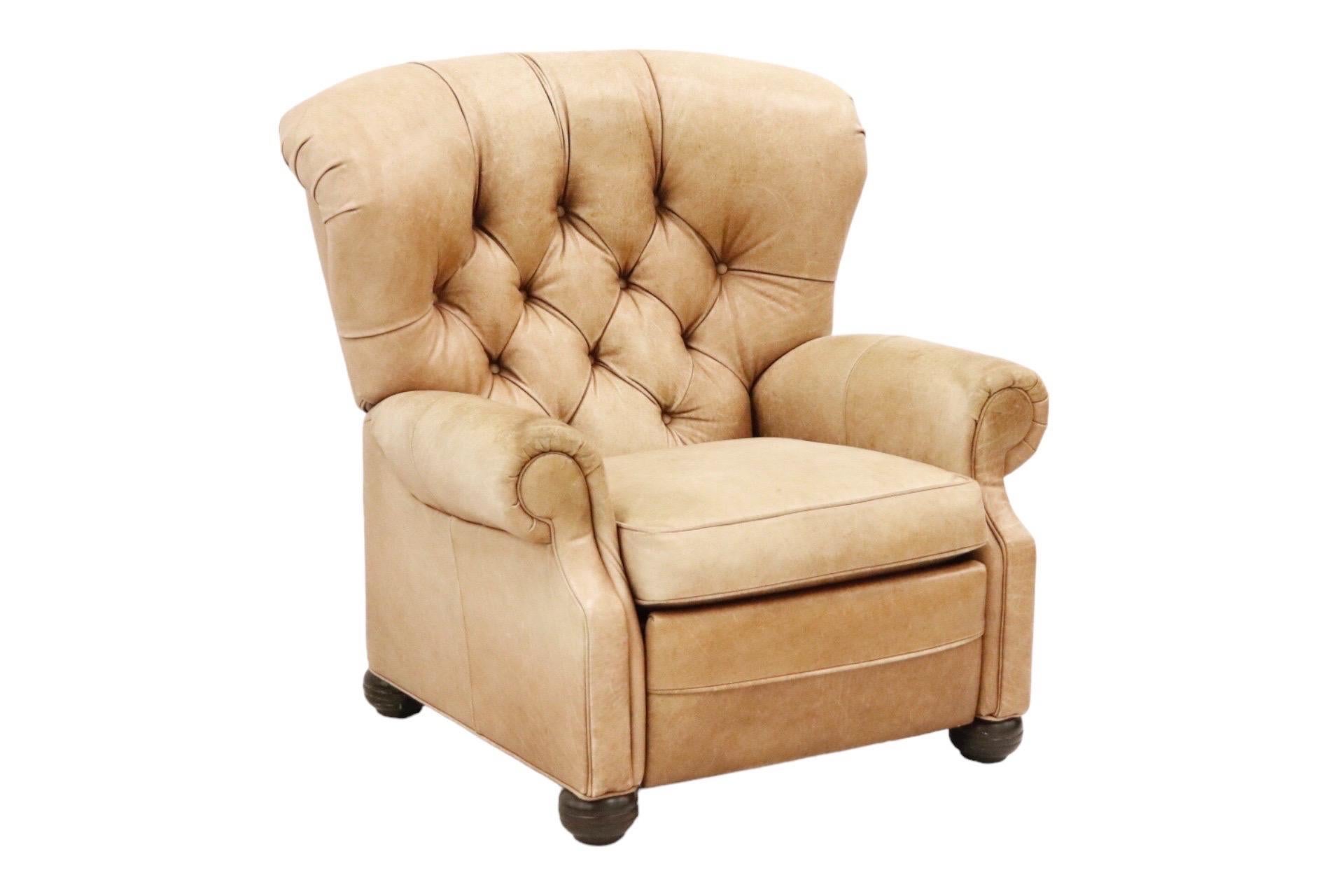 A reclining wingback chair upholstered throughout in brown leather. The inside back is diamond button tufted, and reclines, and the front panel of the chair lifts to become a foot rest. The chair is framed with outward rolled panel arms and finished
