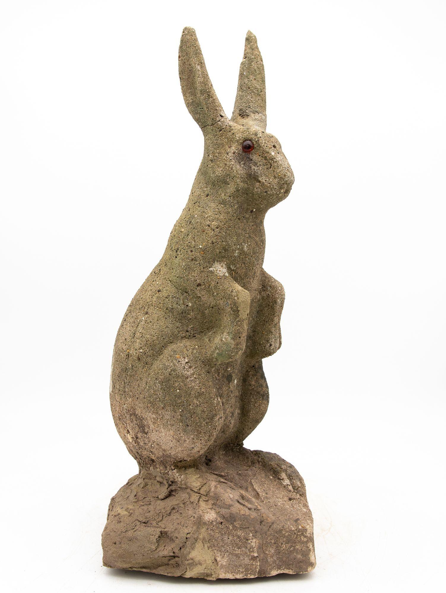 Charmant ornement de jardin français du 20e siècle représentant un lapin assis, les pattes avant relevées. Fabriquée en pierre reconstituée, cette pièce présente un corps détaillé, des oreilles à la forme élégante et des yeux en verre ambré