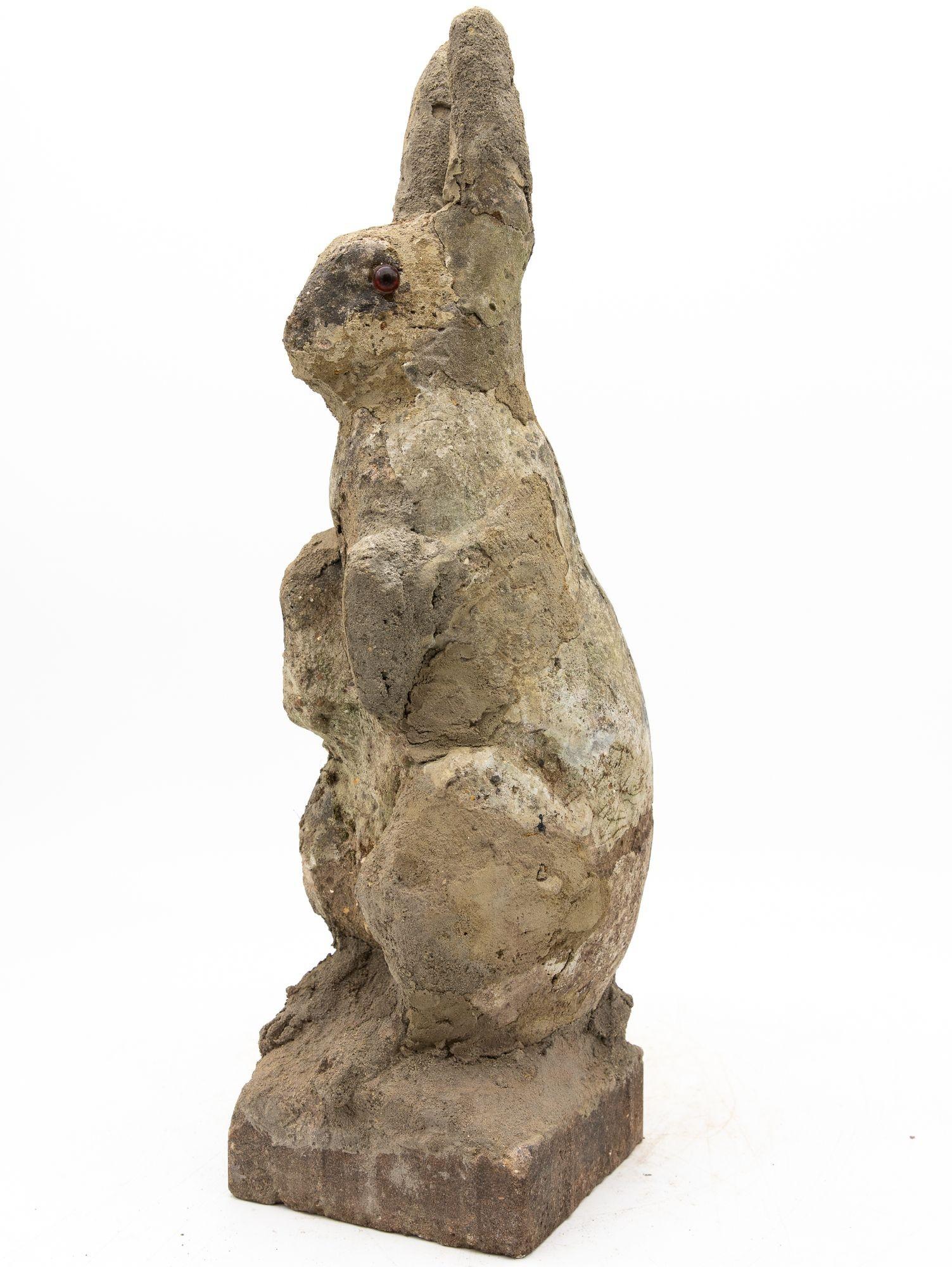 Un grazioso ornamento da giardino francese del XX secolo che raffigura un coniglio seduto con le zampe anteriori sollevate. Realizzato in pietra ricostituita, questo pezzo presenta un corpo dettagliato, orecchie dalla forma elegante e occhi di vetro