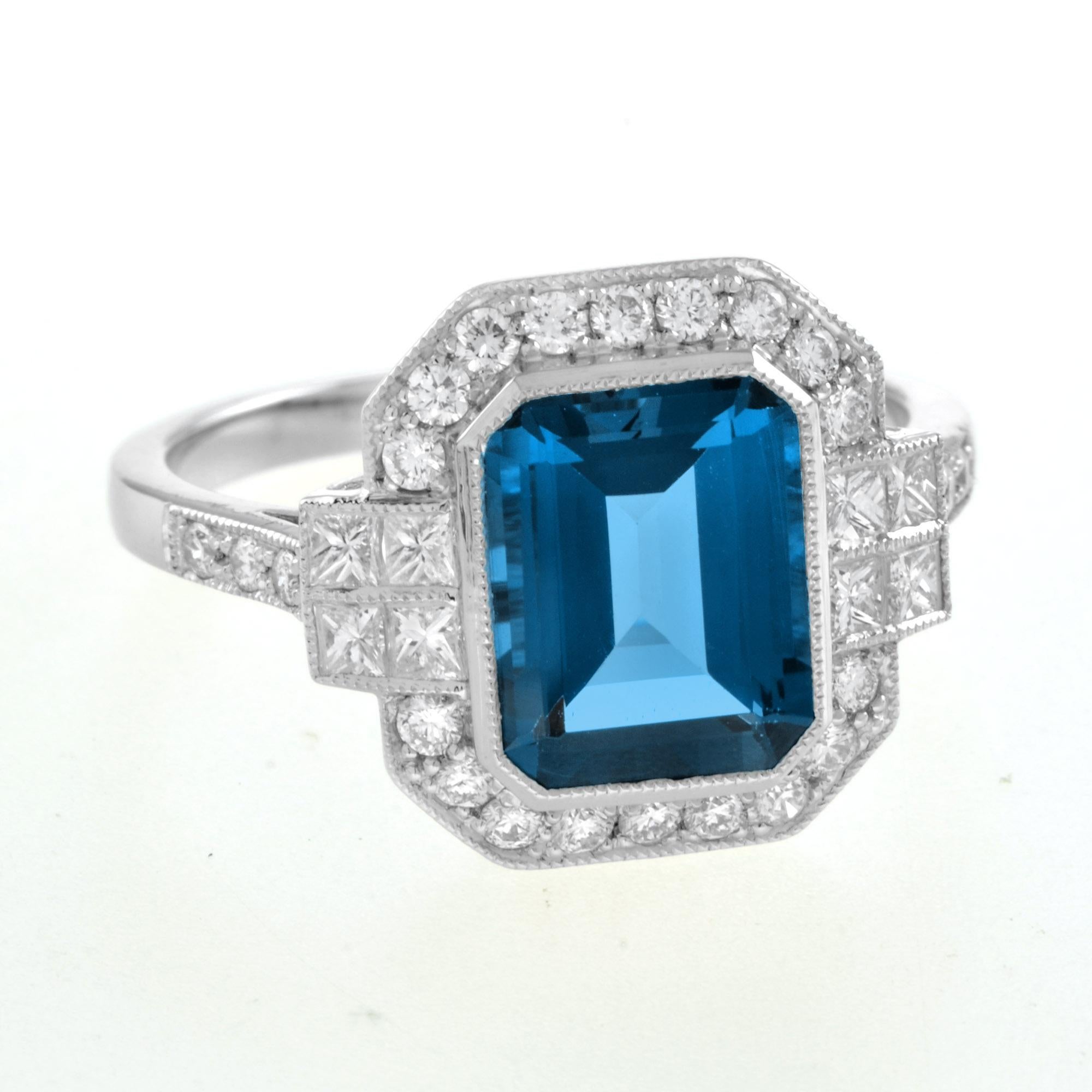 A gorgeous emerald cut London blue topaz is presented in classic Art Deco style. The glorious gemstone radiates from within a sparkling halo of bright round brilliant cut diamonds punctuated east and west with two lines of square diamonds, leading