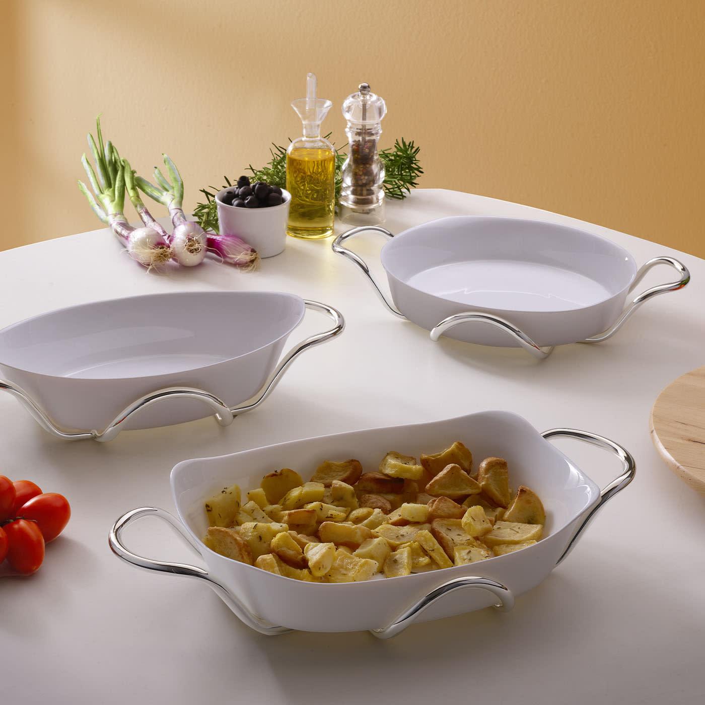 A contemporary spirit clearly conveyed since its fluid lines distinguish this sophisticated ceramic baking dish with brass holders. Enriched with a gleaming silver plating, the cylindrical structure flaunts sinuous curves that well harmonize with