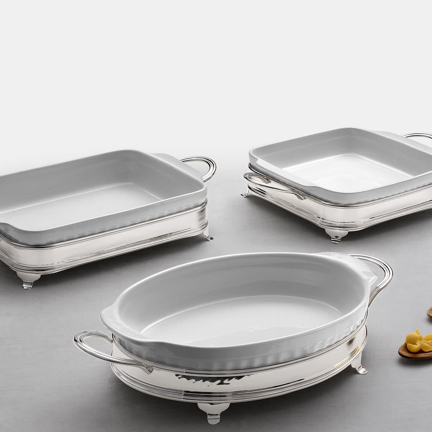 Elegance and luxury define this tableware set comprised of a rectangular white ceramic baking dish and a specific silver-plated brass holder with handles. Showcasing a gleaming finish, the holder comes complete with tiny feet allowing for the baking