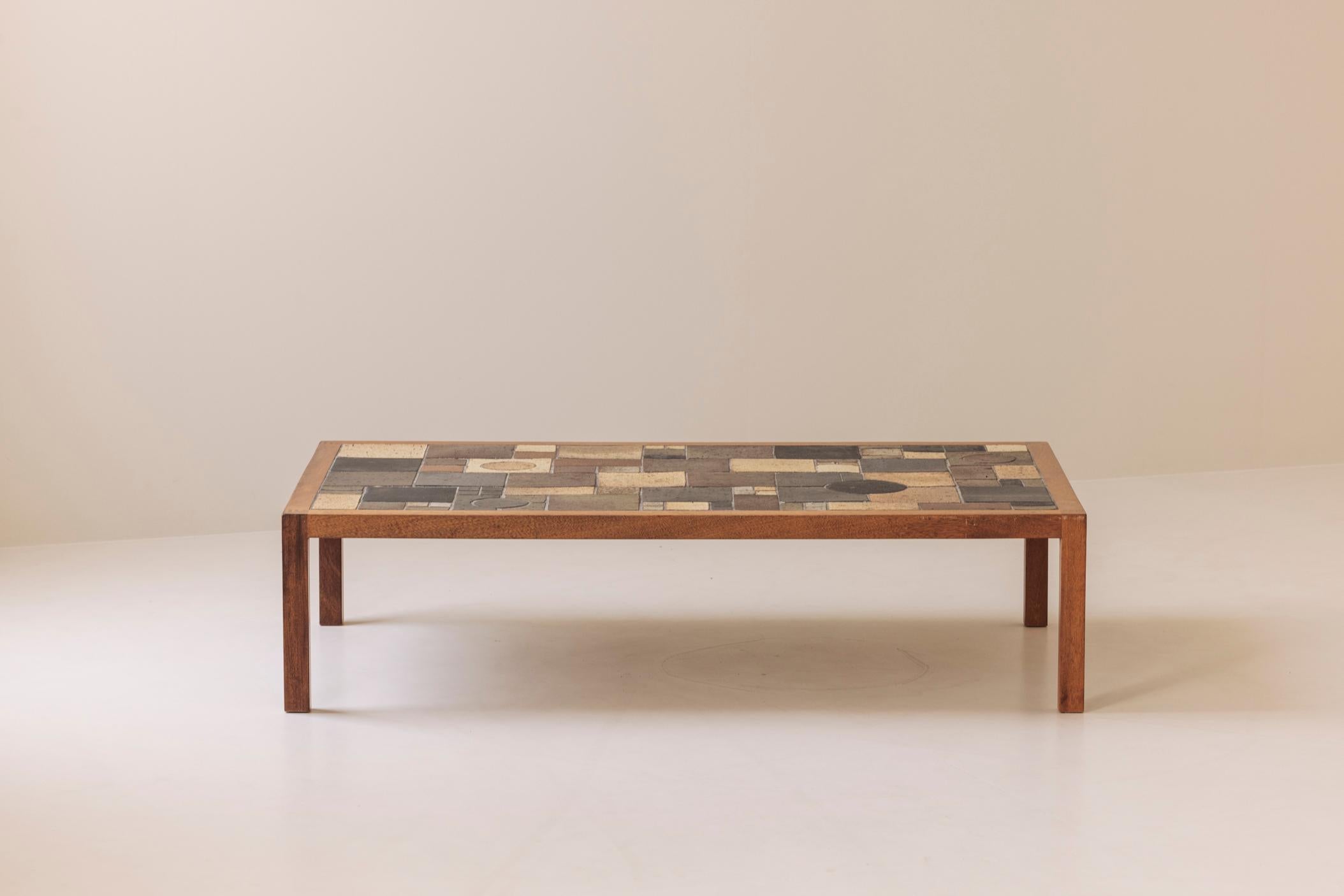 Elegante mesa de centro rectangular de origen danés de los años sesenta. La superficie está incrustada con un mosaico abstracto de azulejos de gres esmaltado en tonos terrosos de marrón, beige y carbón. Cada baldosa tiene un dibujo y una textura