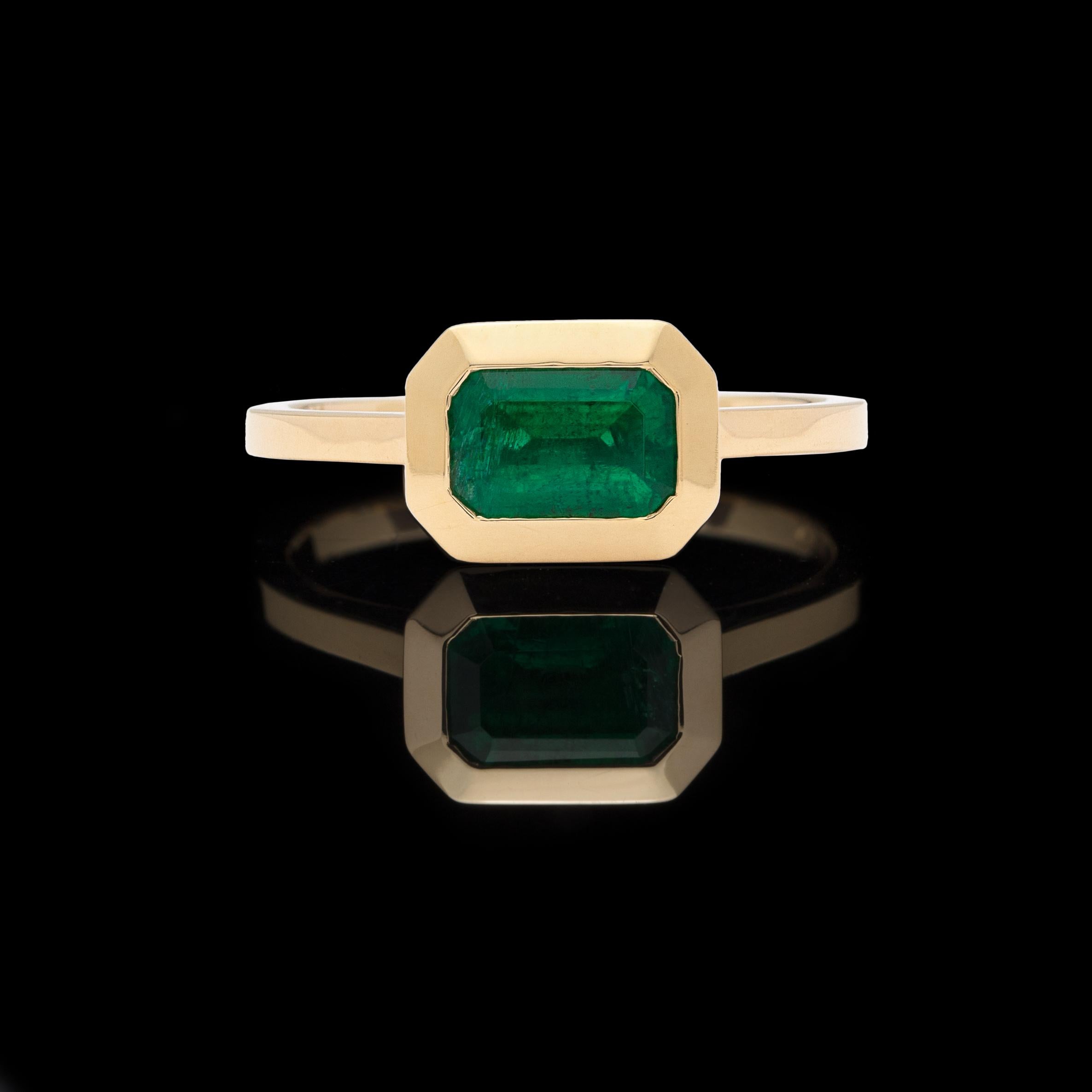 Elegant and charming, this 18k yellow gold ring features a vibrant green rectangular-cut emerald weighing 0.87-ct., horizontally bezel-set in a contemporary custom design. The ring weighs 3.3 grams and currently fits a 5 3/4 finger size, with easy