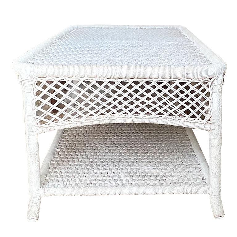 A long vintage French outdoor coffee table. Created from a white rope-like wicker material, this piece is perfect for outdoor gatherings. It is rectangular and long with a low bottom shelf for storing magazines, blankets, or any other items that are