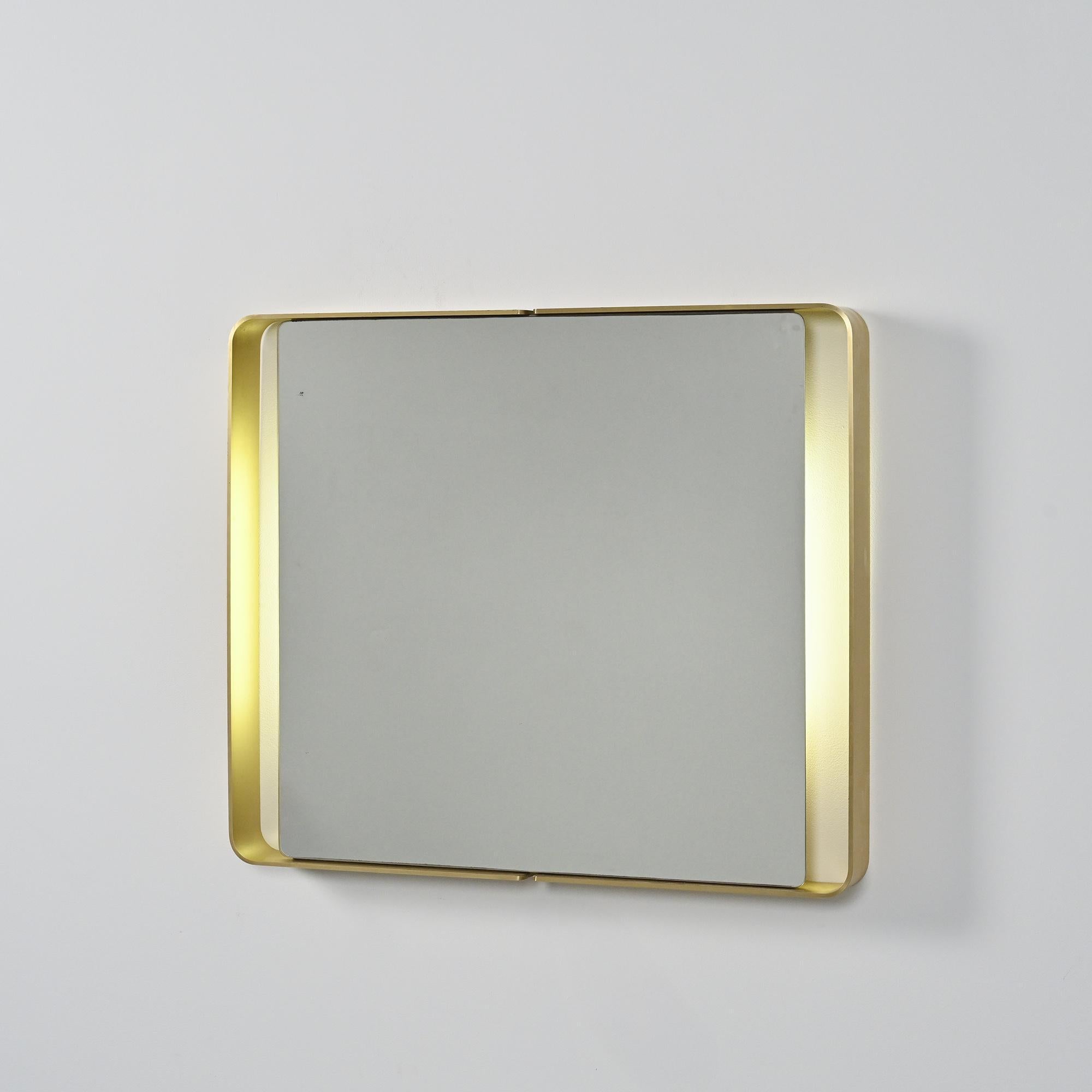Miroir rectangulaire lumineux des années 1970, encadré d'une structure en métal doré plié formant une ligne continue aux angles doucement arrondis.

 Sa silhouette épurée et élégante, caractéristique du design des années 70, en fait une pièce