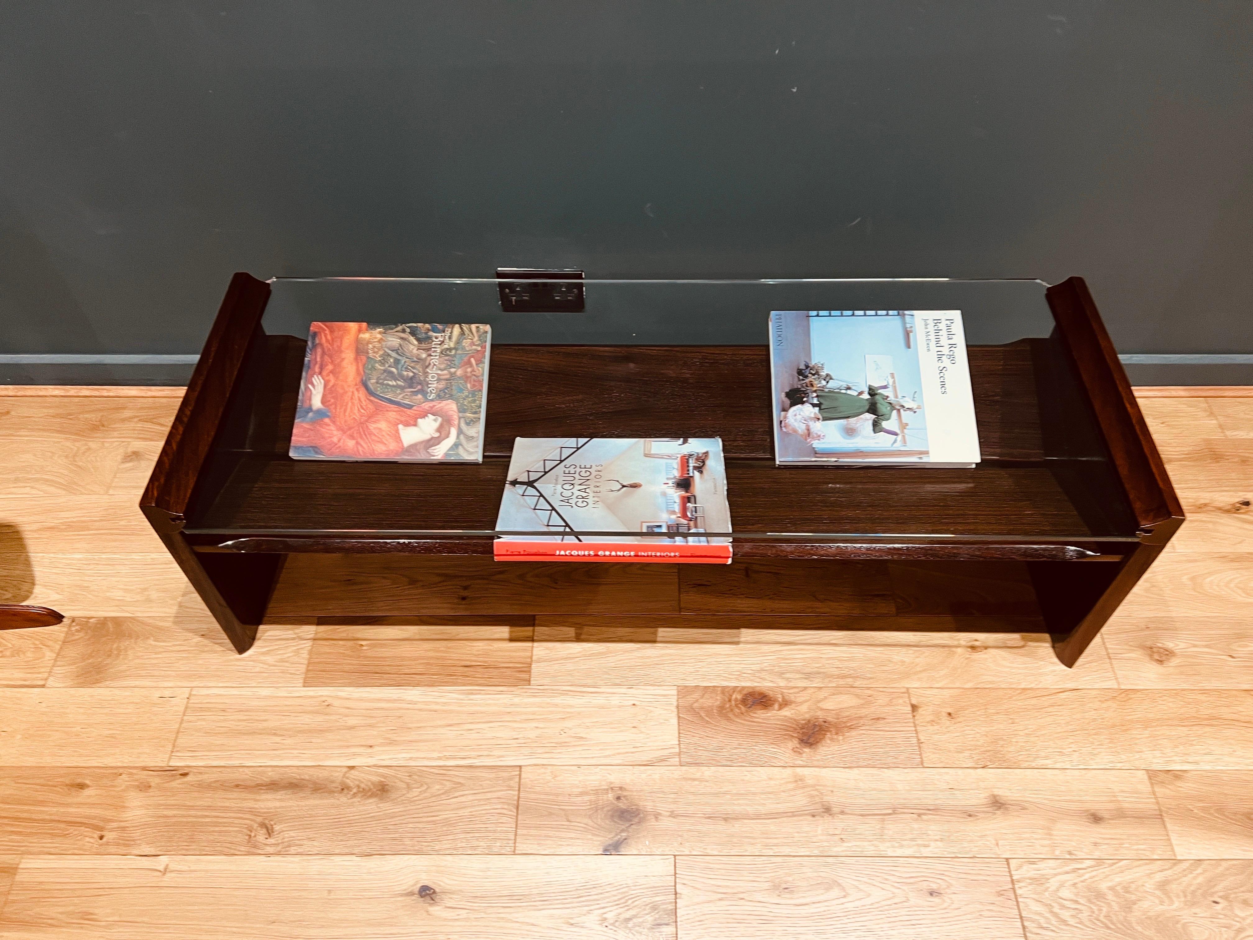 Table basse rectangulaire en placage de bois foncé et verre taillé, avec deux plateaux en bois sous-jacents pour exposer des livres ou des magazines. .
Produit en Italie dans les années 1960 