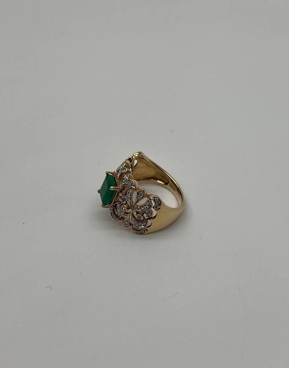 Dieses exquisite Stück hat ein auffälliges Design in Gold. Das Herzstück ist ein leuchtend grüner, rechteckiger Smaragd, der sicher in eine vierzackige Fassung eingesetzt ist. Der Stein ist von einem komplizierten, durchbrochenen Muster umgeben, das