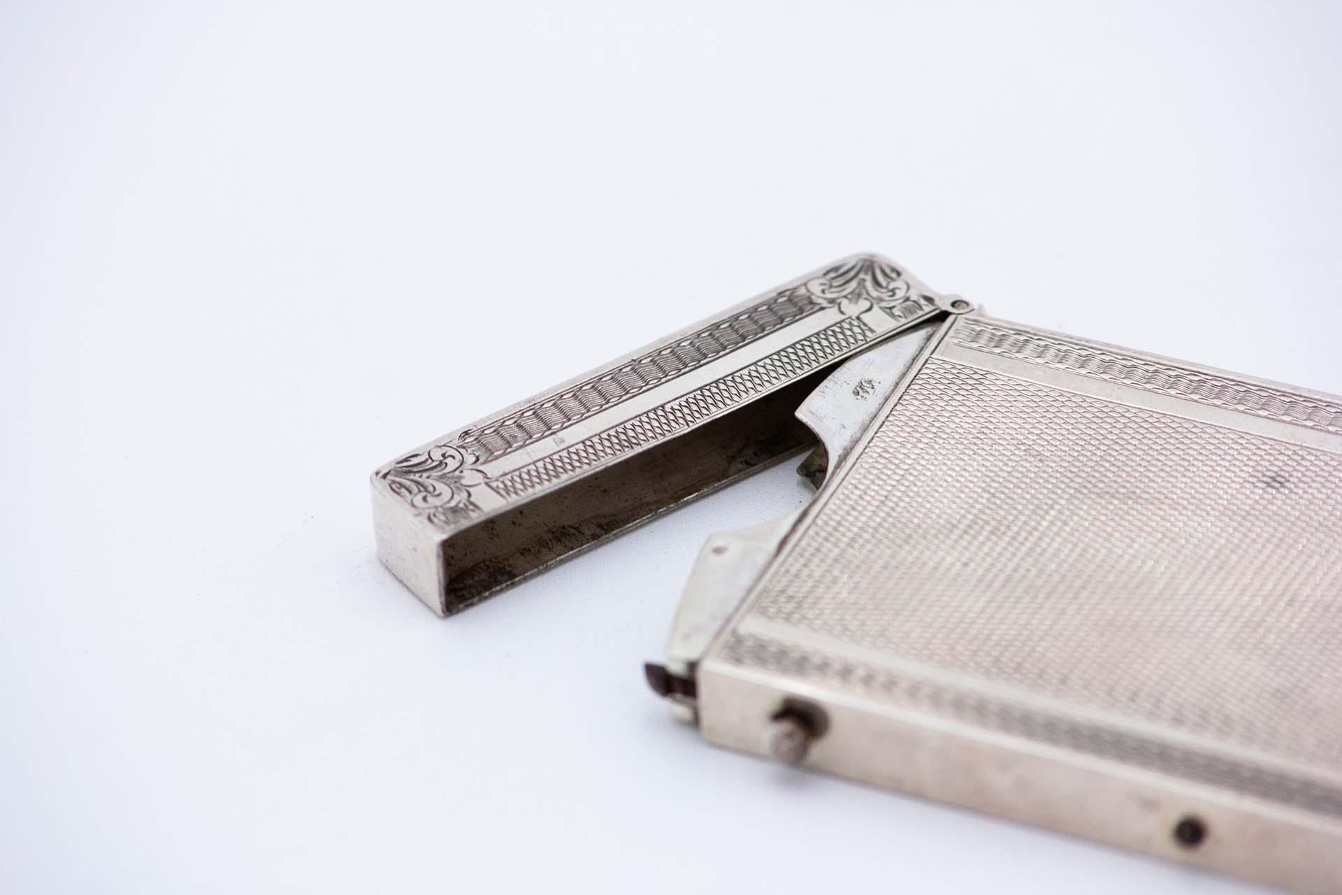 Description: Rectangular guilloche silver card case with a card surrounded by engraved floral motifs, and a frilled frame with fleurs-de-lis at the corners. Metal: Silver. Origin: European. Mark: Unreadable. Weight: 79.24 grams. Dimensions: