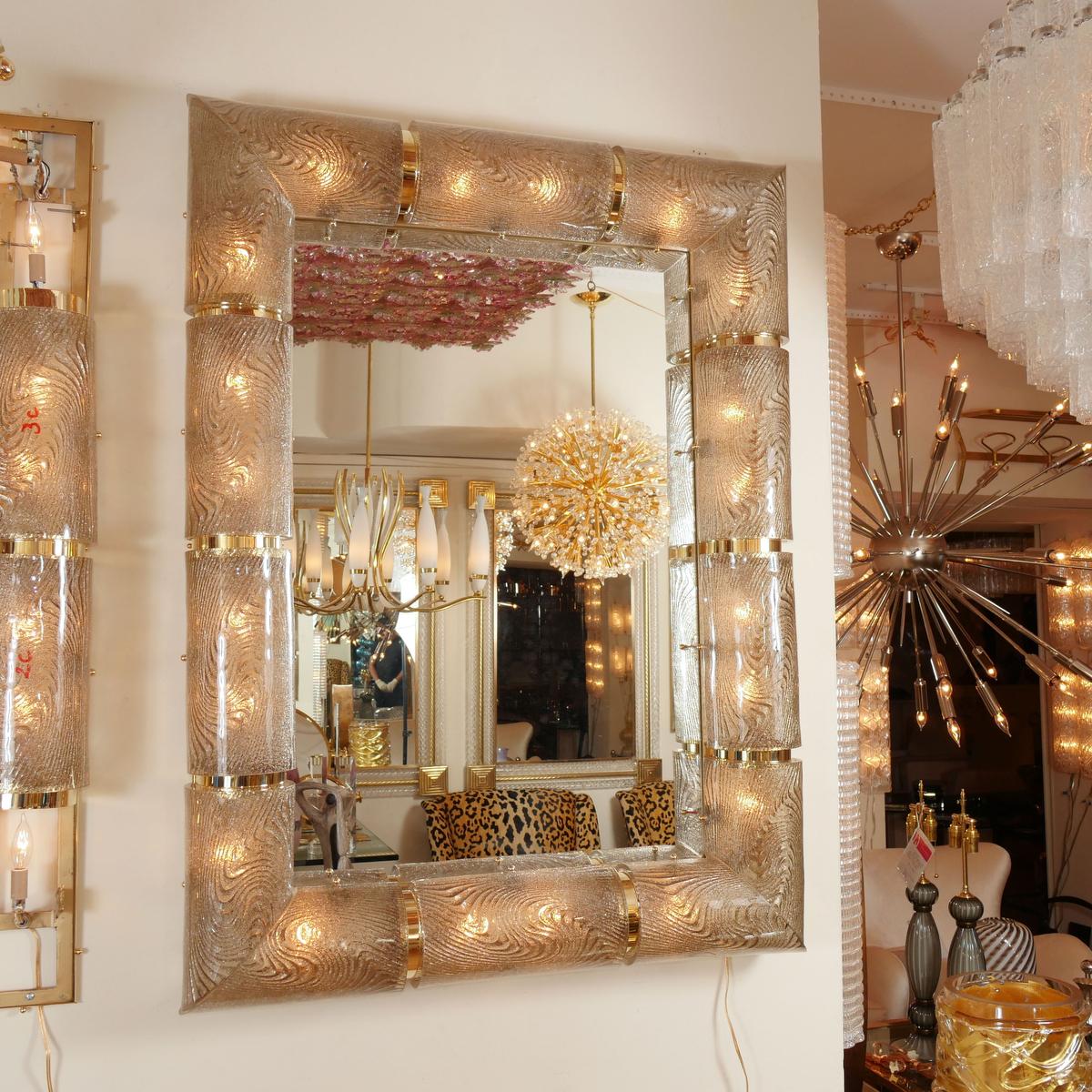 Rectangular illuminated mirror with textured glass surround and decorative brass details.