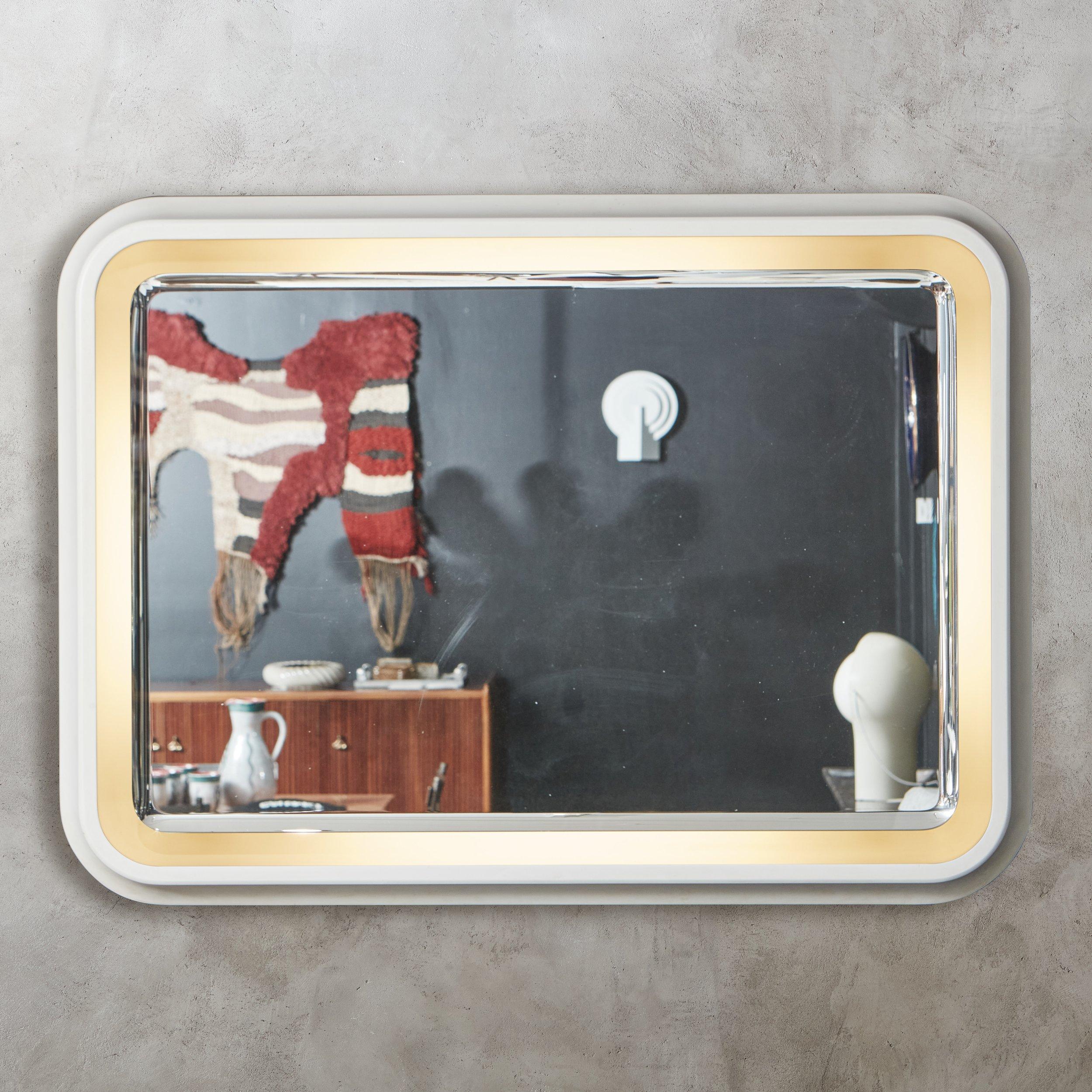 A 1970s Italian mirror featuring an ivory rectangular acrylic frame with curved corners. This piece has a backlit mirror with a beveled edge, which appears to float within the frame. When lit, this mirror emits a warm, ambient glow. Unmarked.