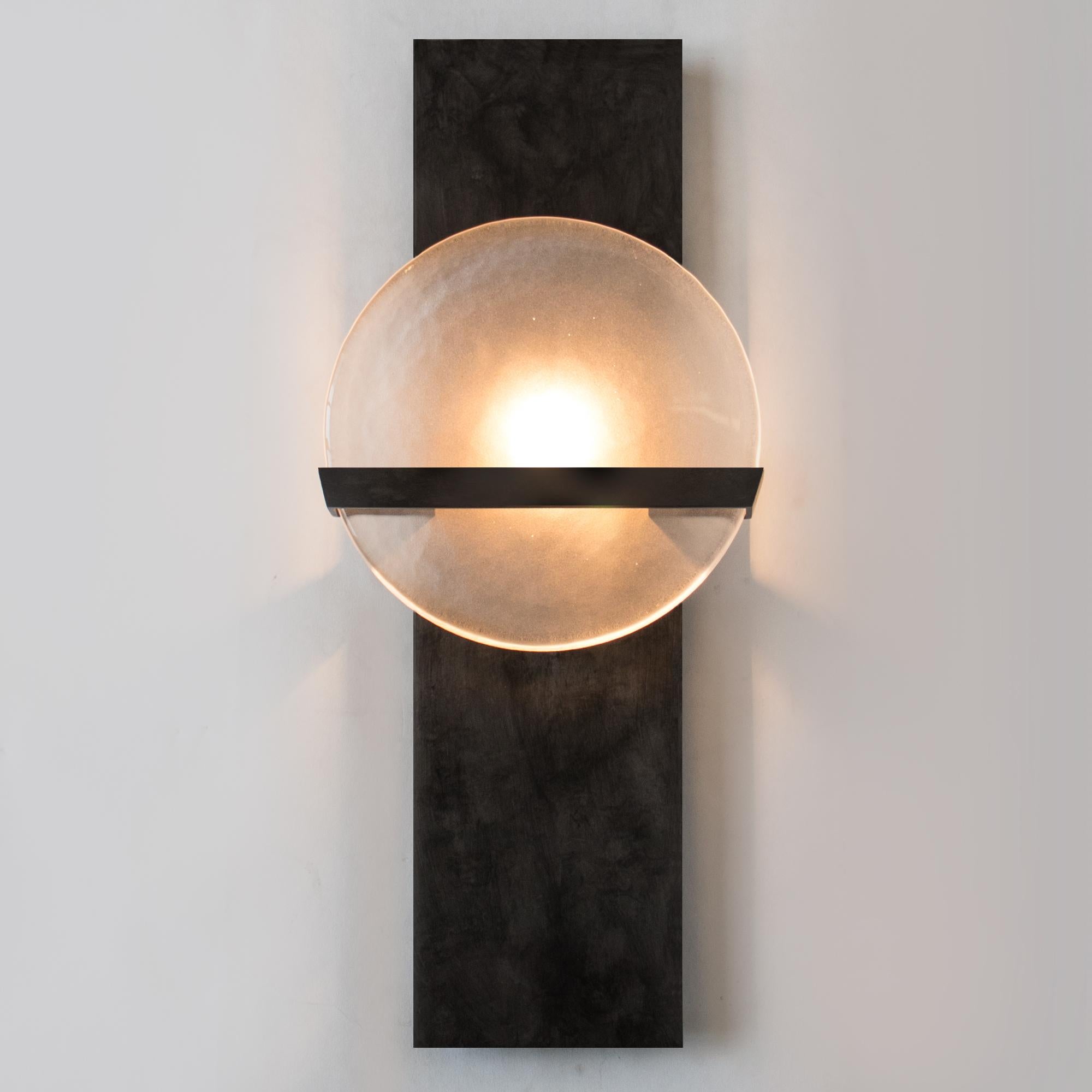 The LUNETTE wall sconce is composed of a cold rolled steel body with a delicate armature projecting a frosted cast glass diffuser. This sconce is available in a variety of plated finishes and cast glass textures. The LUNETTE Wall Sconce is
