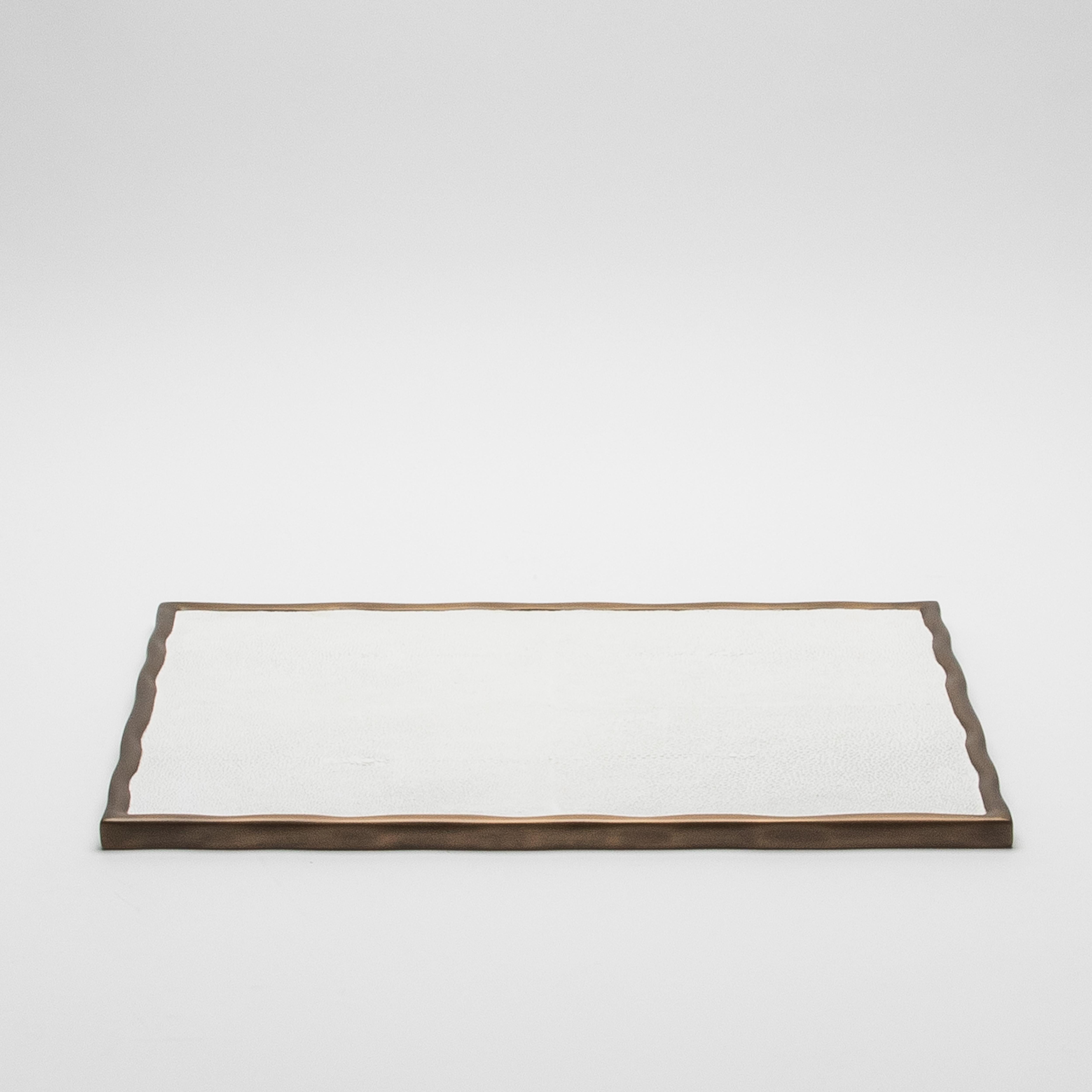 The Rectangular Melting Tray by R&Y Augousti in white shagreen exudes refined sophistication and meticulous craftsmanship. Encased in bronze patina brass with an organically flowing melting border, this tray merges timeless elegance with modern