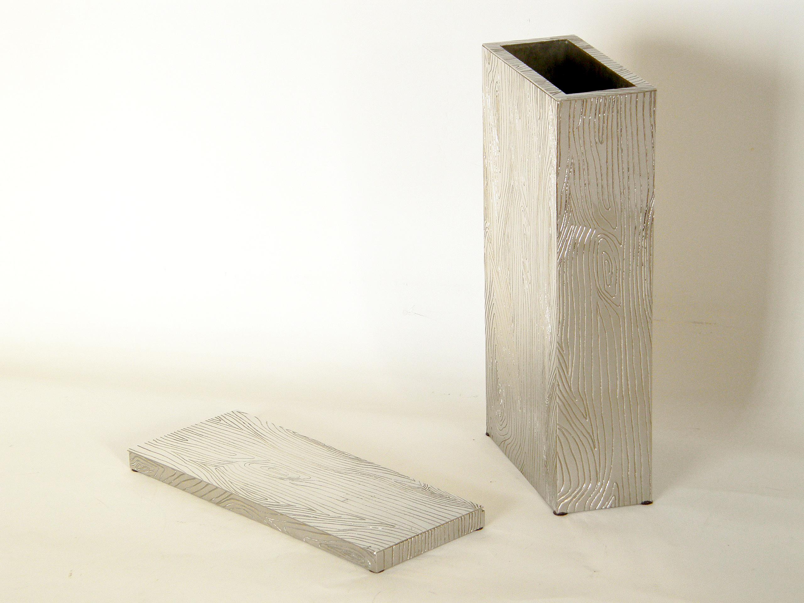 This unusual metal vase and matching box have an impressed faux bois pattern. The shallow box has an attached, hinged lid. They both are rectangular in shape, and the use of metal and the highly polished finish are well suited to their crisp,