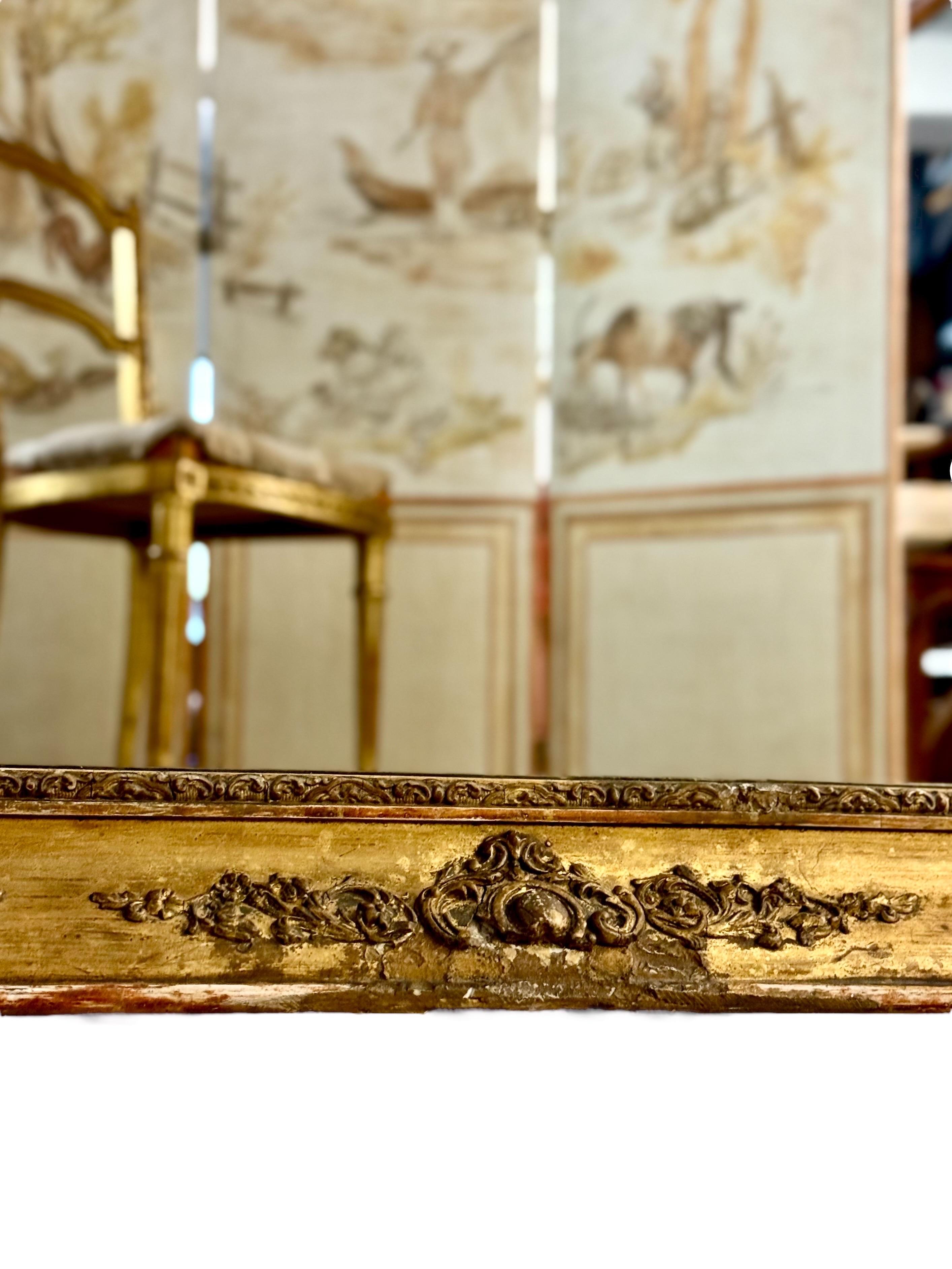 This rectangular French Napoleon III period mirror (circa 1960) exemplifies Second Empire elegance and opulence with its carved and gilded wooden frame lavishly adorned with intricate Rococo-inspired floral and scroll motifs. 

The hand-carved