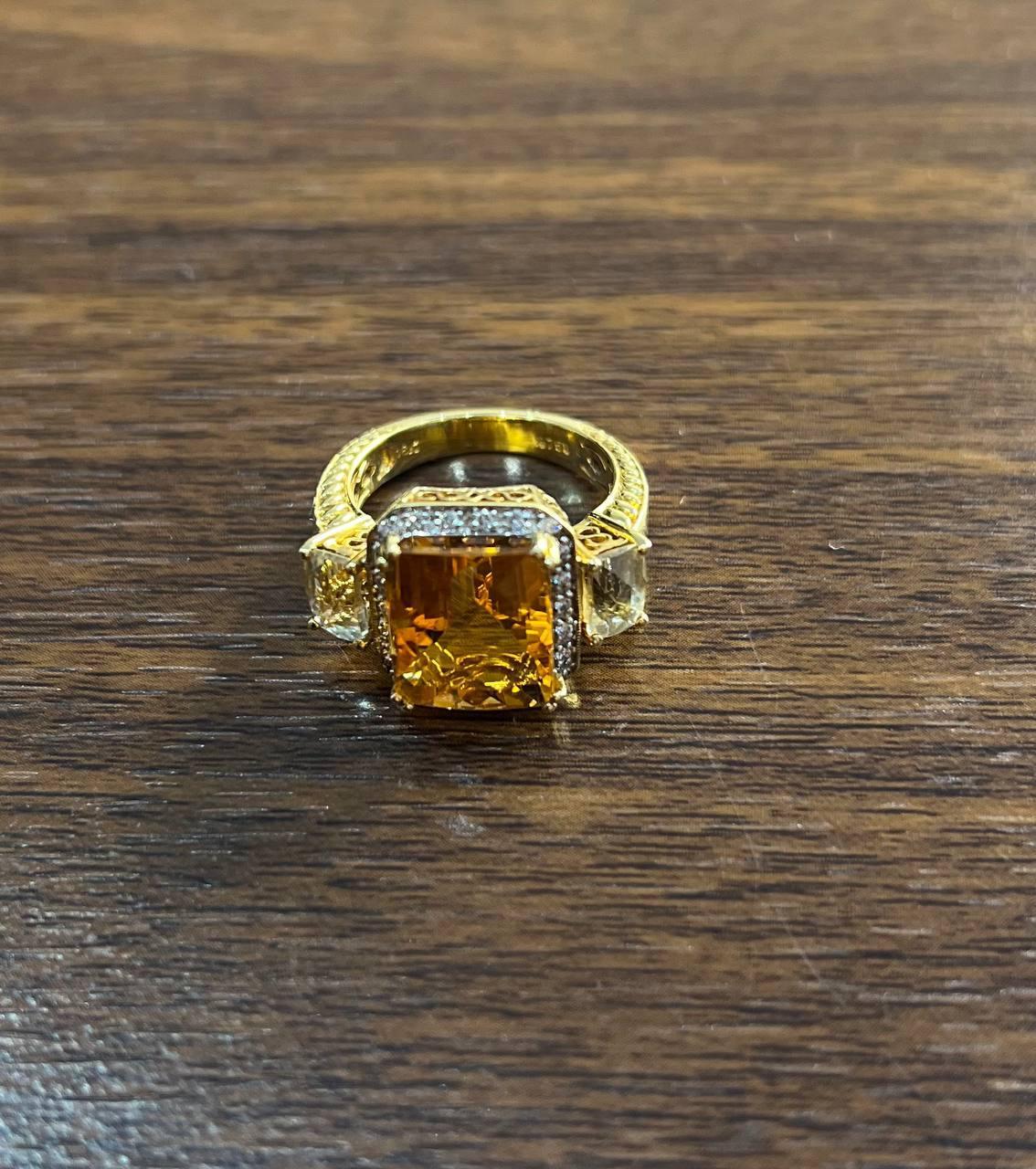 Questo anello a fascia è realizzato in oro giallo 18 carati. Presenta un grande e vibrante citrino arancione rettangolare, incorniciato da un'aureola di piccoli e scintillanti diamanti bianchi e pietre laterali di quarzo.

La fascia è ornata da un