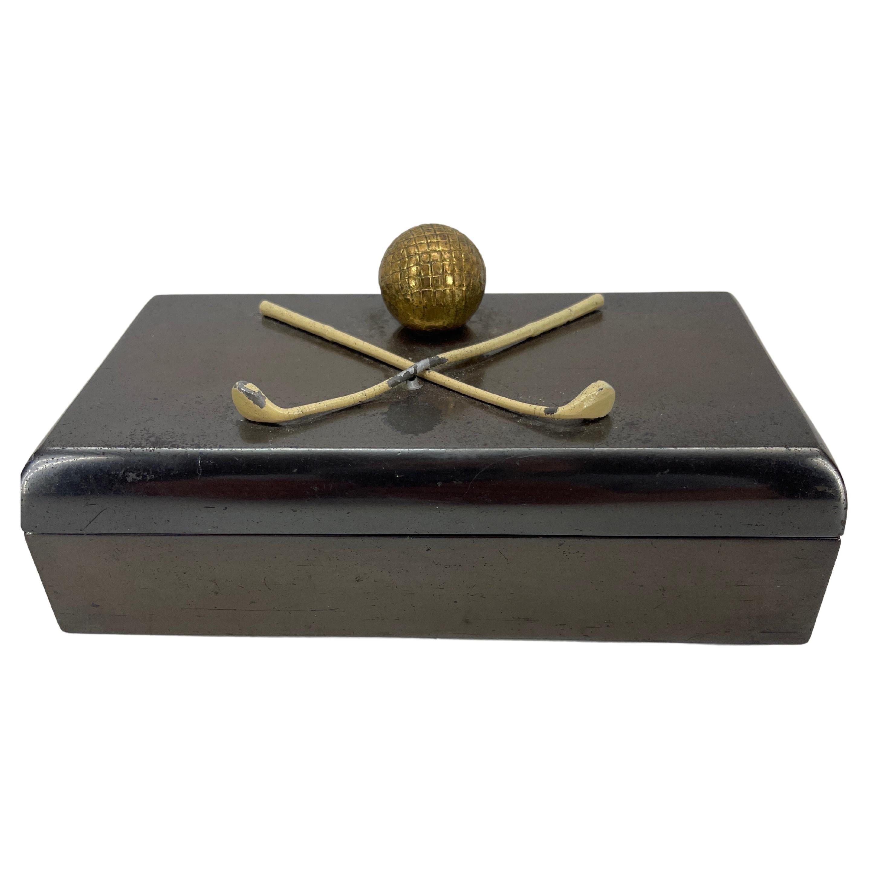 Art Deco cigarette or jewelry box in thick heavy patinated bronze with white painted golf clubs and gilded golf ball as lid decoration. The interior of the box has two compartments made from later installed faux marble linings. These are loose