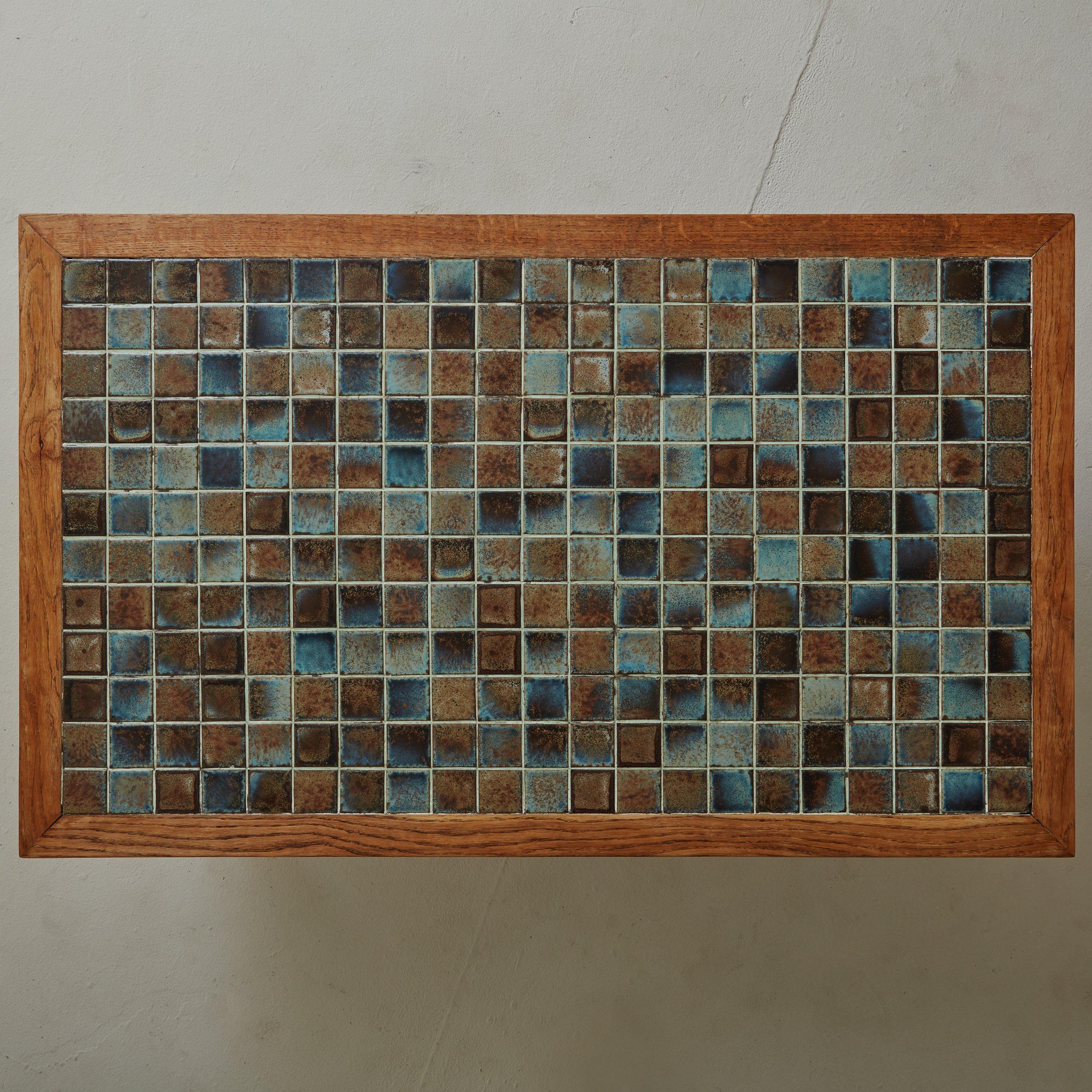 A 1970s Danish coffee table featuring a rectangular pine wood frame with a glazed ceramic tile top in a gorgeous range of teal, blue and brown hues. This elegant table stands on four black iron block legs and sits low to the ground. Unmarked.