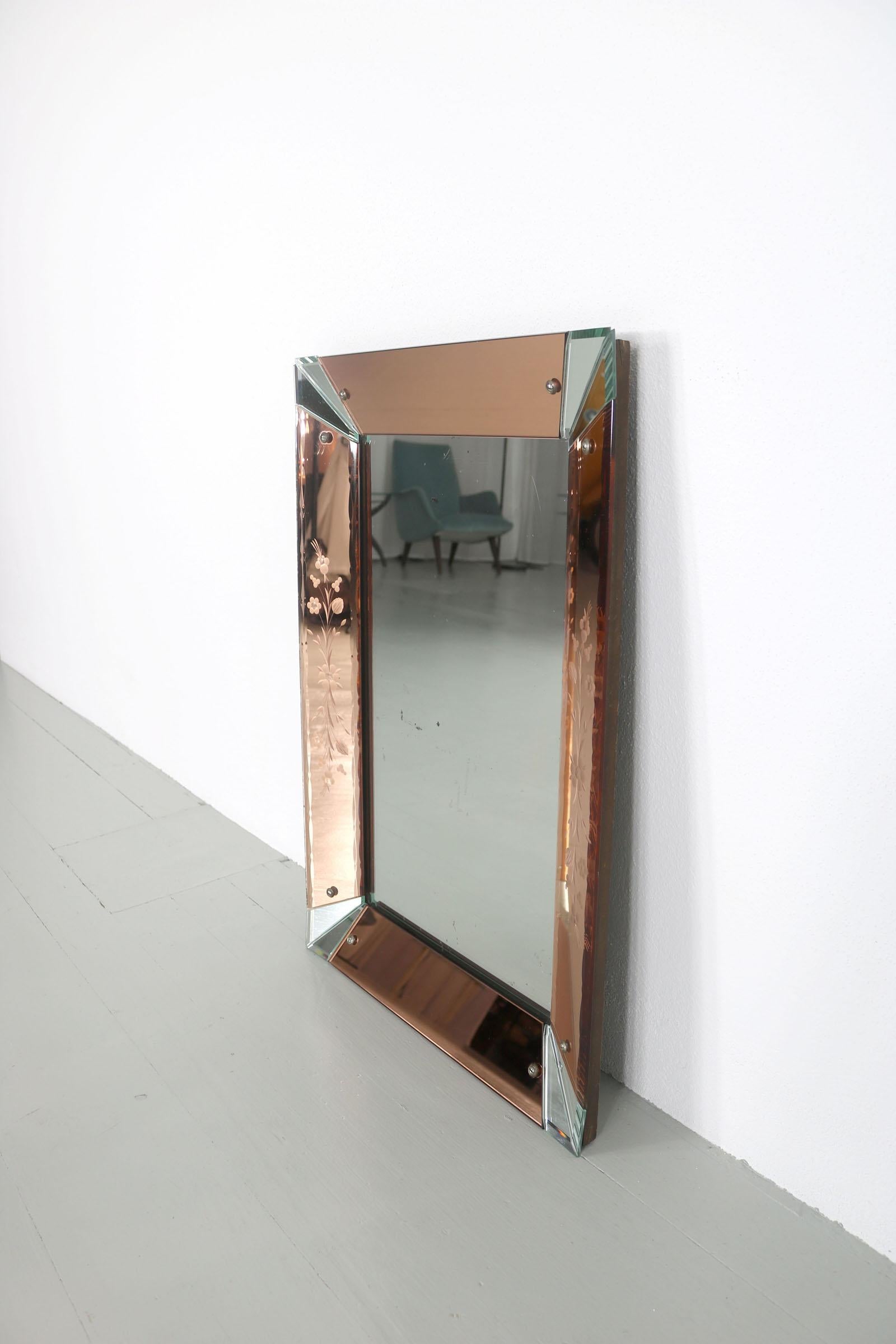 This rectangular mirror has a mirror glass frame on the outer edge of the mirror. The corners are glassy-transparent and the areas in between are made of old rose colored glass that has engravings in the form of floral patterns.