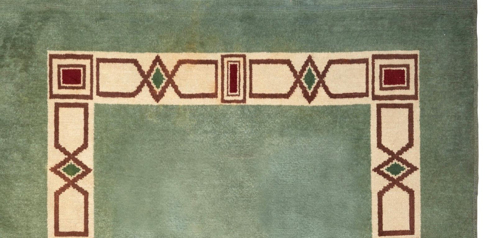 Rectangular woolen rug with geometrical green, burgundy and off-white decoration on a celadon green background.

Signed Leleu in a corner.