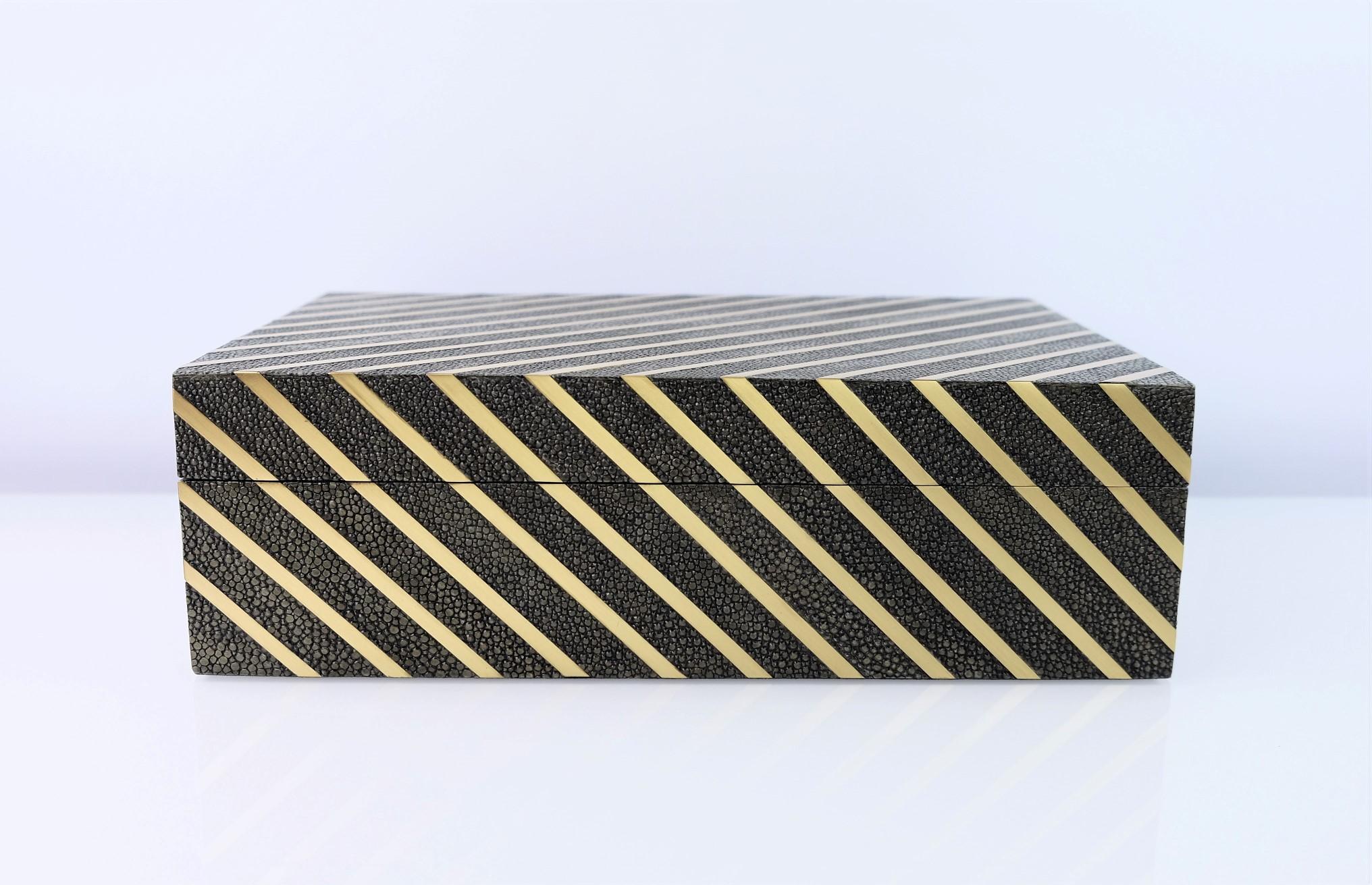 This modern box by Ginger Brown is handcrafted with shagreen and brass trims striping.

The box is hinged and the interior is lined with a high quality black microsuede.

The color of the shagreen is a dark olive green.
 
The dimensions of