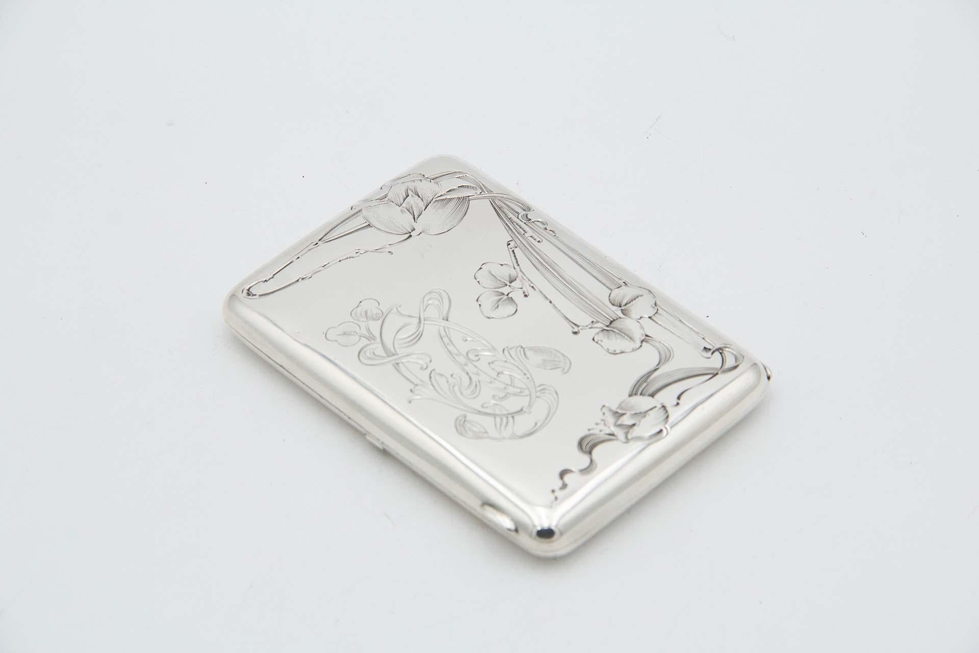 Description: Rectangular silver cigarette case with beveled corners, floral motifs engraved on the hinged lid and gold interior. Metal: Silver. Origin: Russian. Brand: KC. Weight: 137.87 grams. Dimensions: 11cmx1.3cm. Content: 84 zlotys = 875/1000.