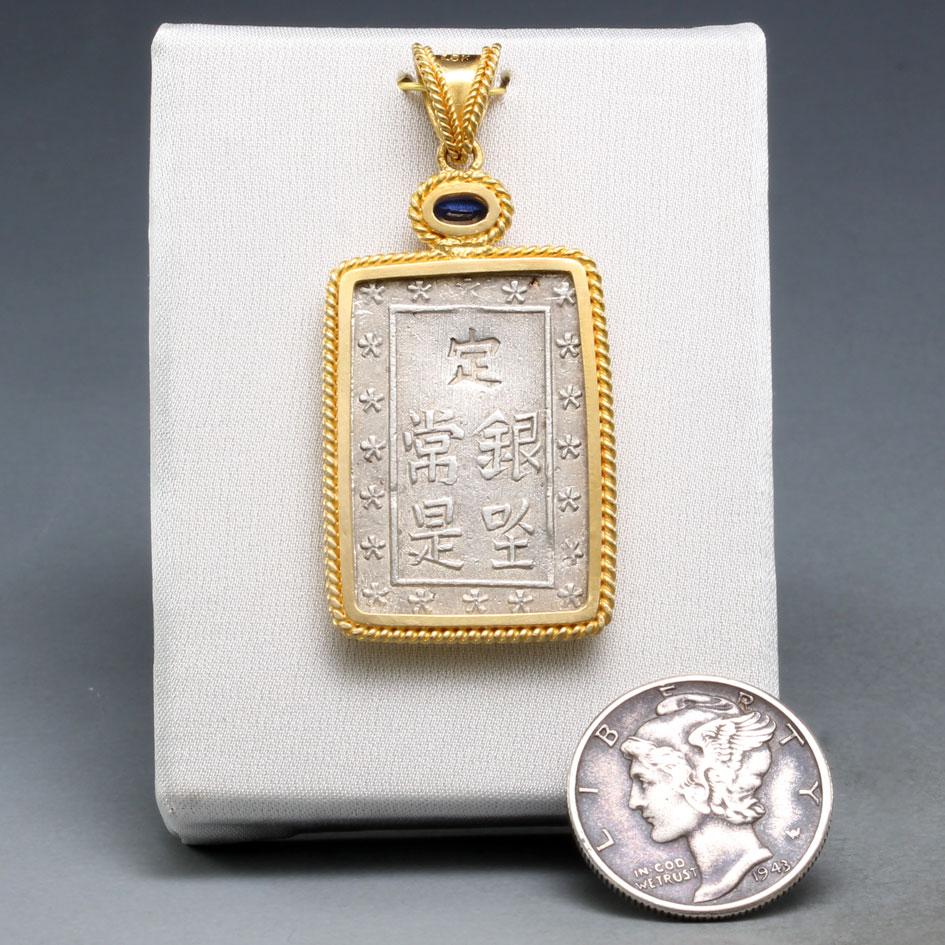 An interesting rectangular silver coin from the last Japanese shogunate, minted in the waning days of their power 1837-1854, is set in classic 18K gold double braid setting with a bright 3 x 5 mm faceted kyanite accent.  The coin is a an 