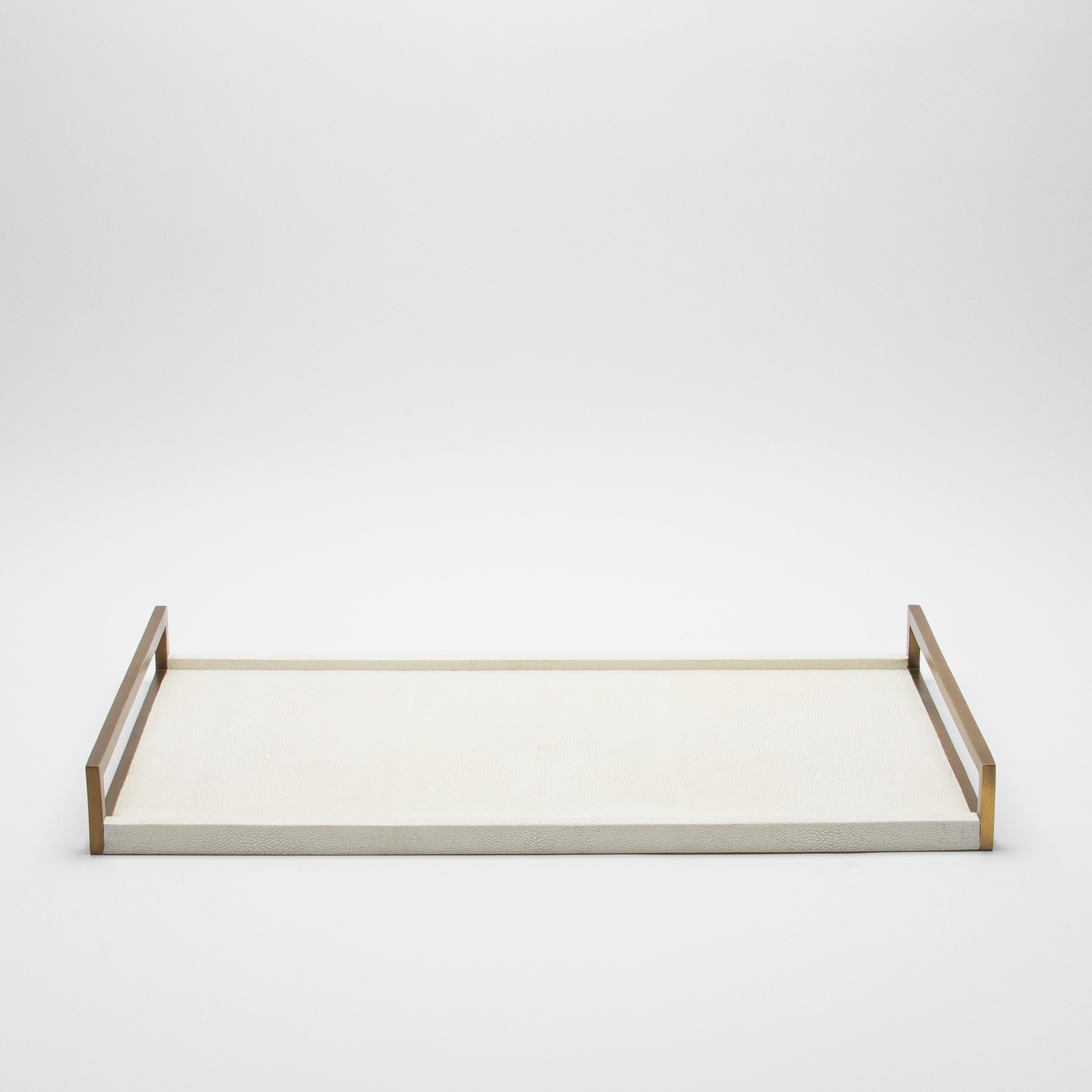 This elegant rectangular tray by R&Y Augousti is a stunning display of luxurious craftsmanship. With its sleek natural cream shagreen surface, it exudes sophistication, while the contrasting bronze patina brass handles add a touch of opulence. Every