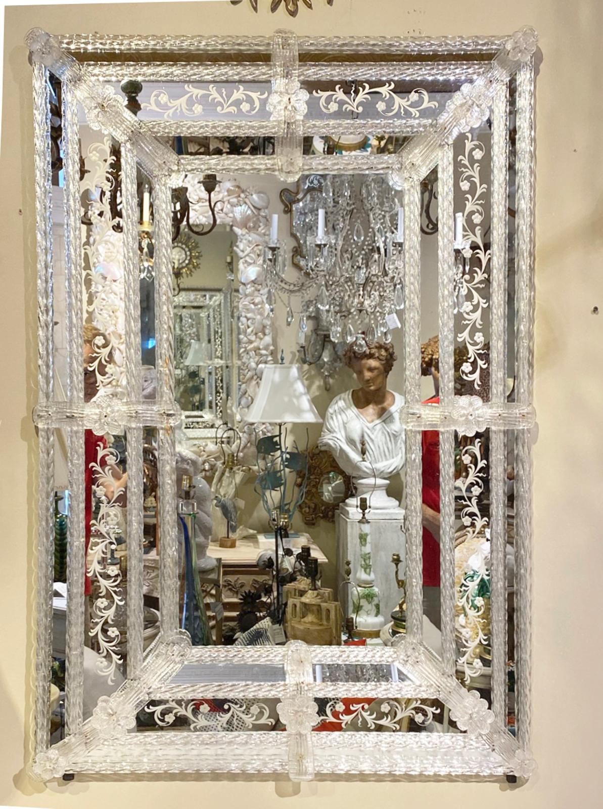 Classic Venetian glass wall mirror, having a central perimeter of clear mirrorplate, in a frame of mirror reliefs, etched with scrollwork; handblown accents of ribbons, ropes, and flowerheads adorn its corners and sides. 

Stock ID: D3078.