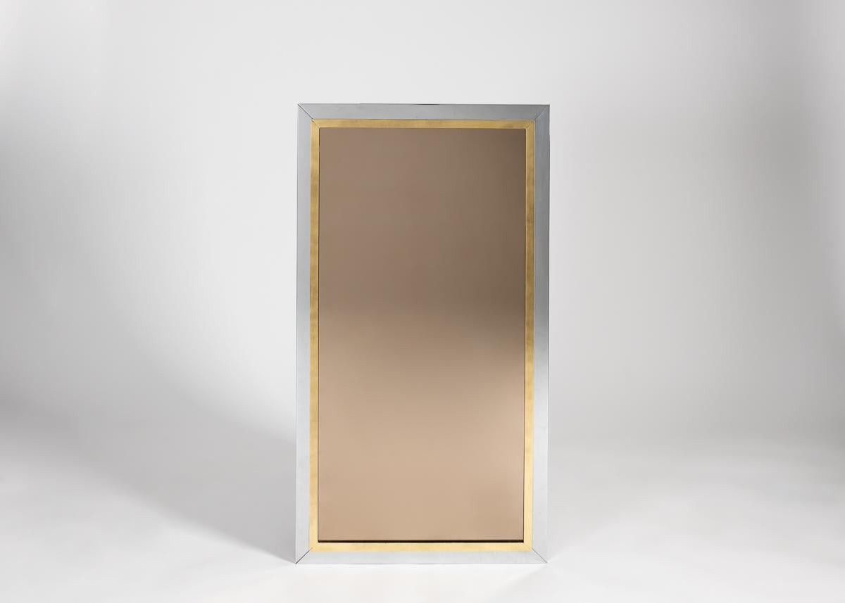Un élégant miroir rectangulaire avec un cadre en chrome complété par une bordure en laiton.