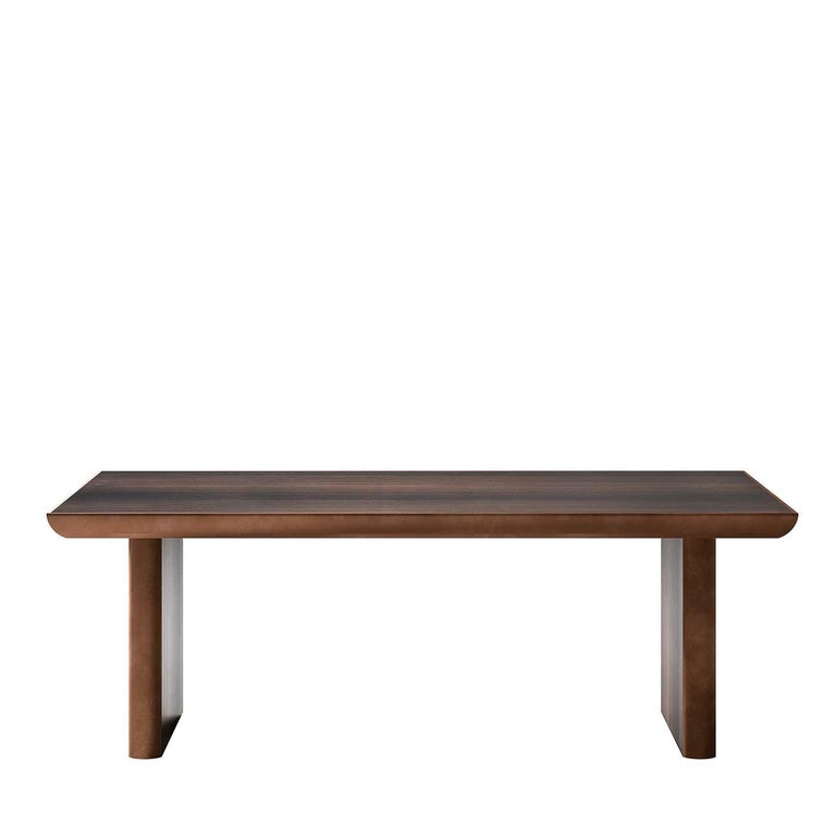 Unique in its simplicity, this dining table disguises a masterful construction under its streamlined rectangular shape. A subtle balance of geometries defines the veneered top and legs with a warm, dark finish and metal edges that flaunt a straight