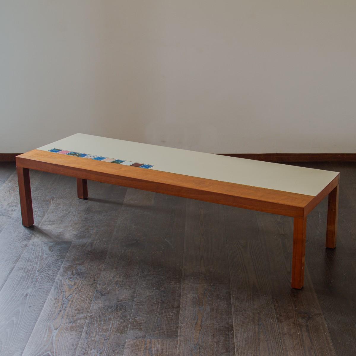 A rectangular wooden coffee table with three quarters of the top being white laminated and inset with colourful enameled tiles. The rest of the top and the legs are stained wood and seperated from the laminate with a brass inset strip. circa 1960s