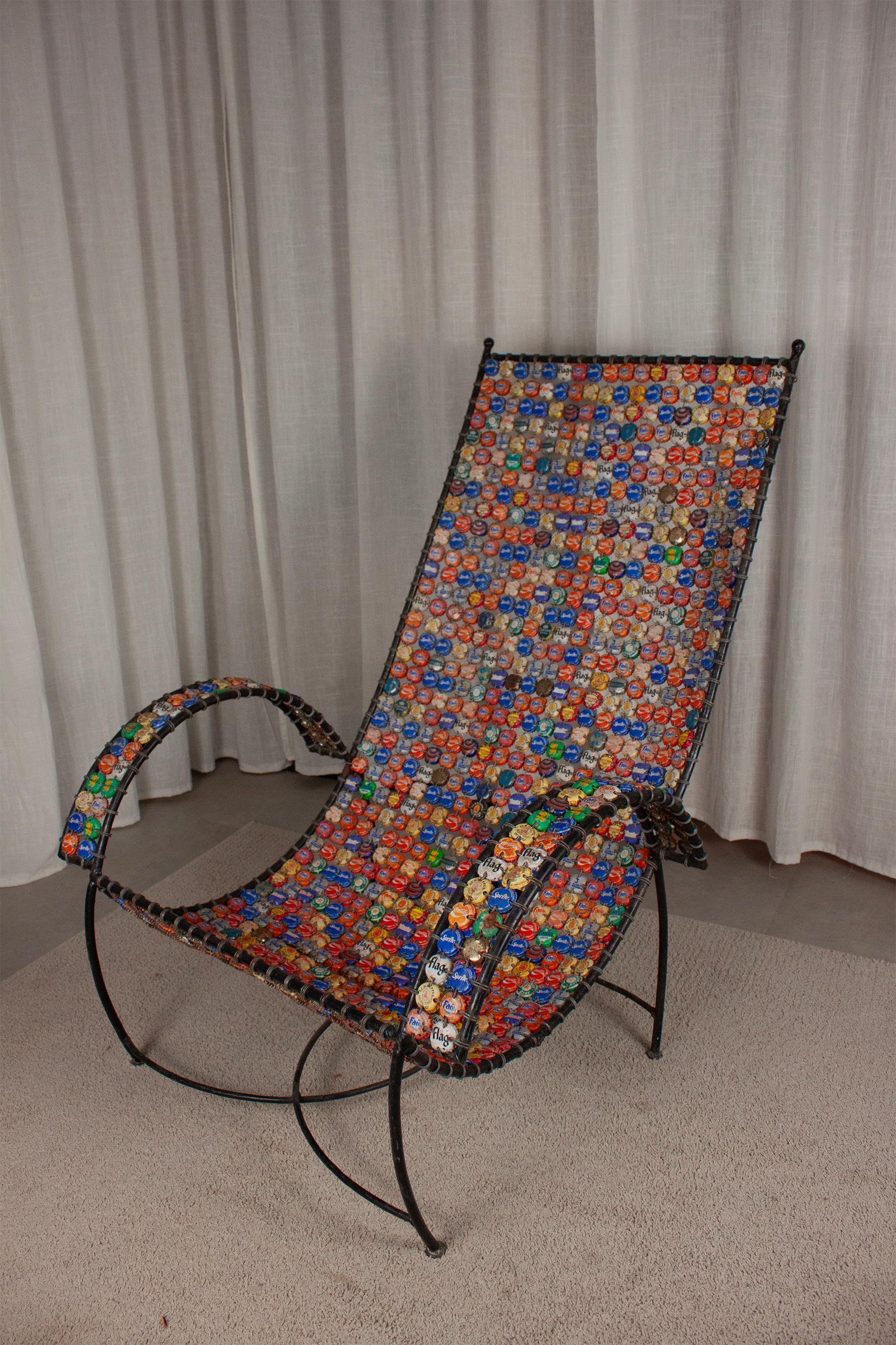 Ein handgefertigter, recycelter Stuhl auf einem Eisenrohrrahmen, dessen Sitz und Rückenlehne aus Hunderten von geflochtenen oder verdrahteten Flaschenverschlüssen besteht. Unter den Caps befinden sich gängige Sodamarken sowie gewölbte Caps mit