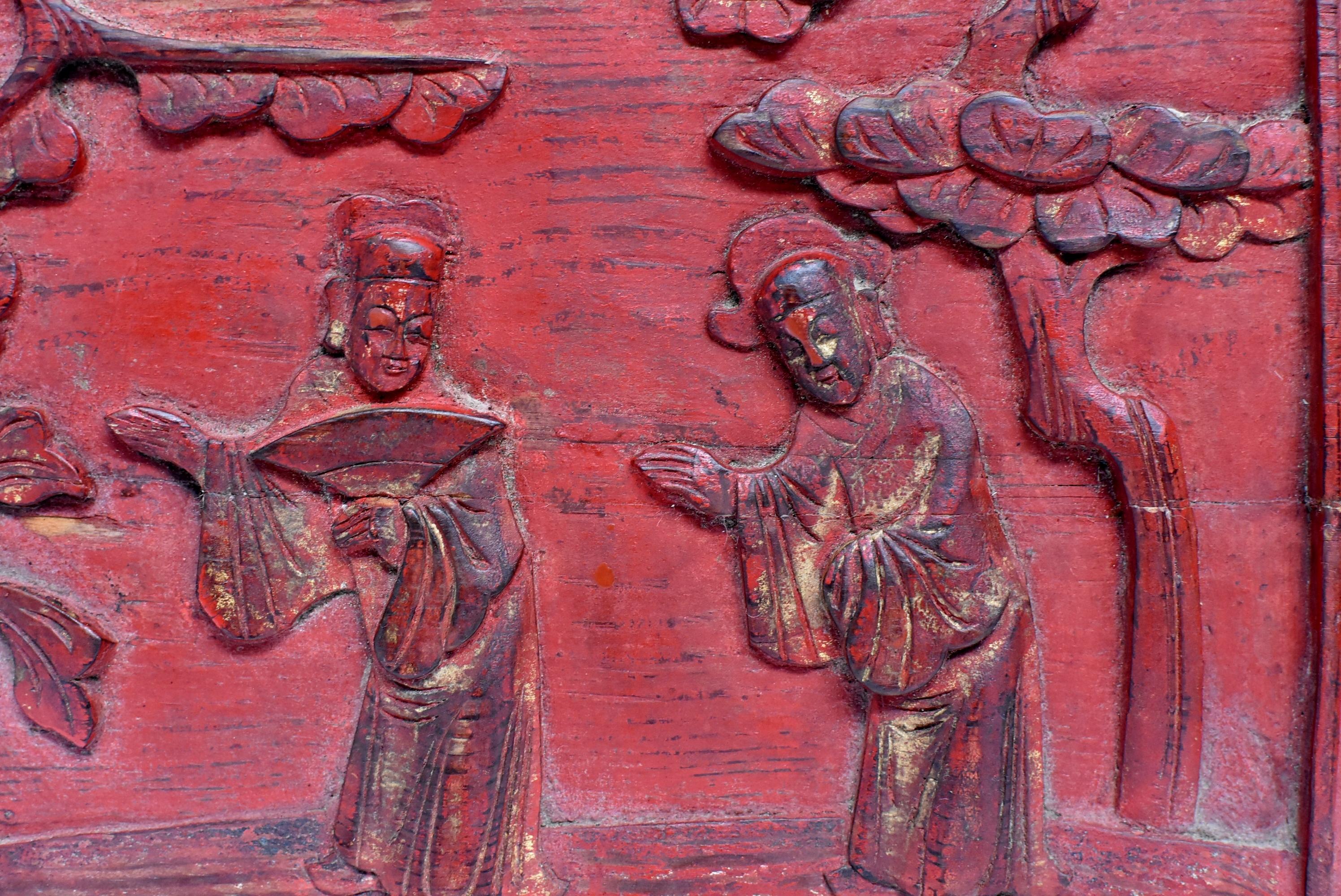 A red lacquered 19th century wood carving panel featuring two friends in their traditional official robes yielding the path for each other. Evergreen pine tree is symbolic of long lasting friendship. A partial peony hints prosperity. Hand carved.