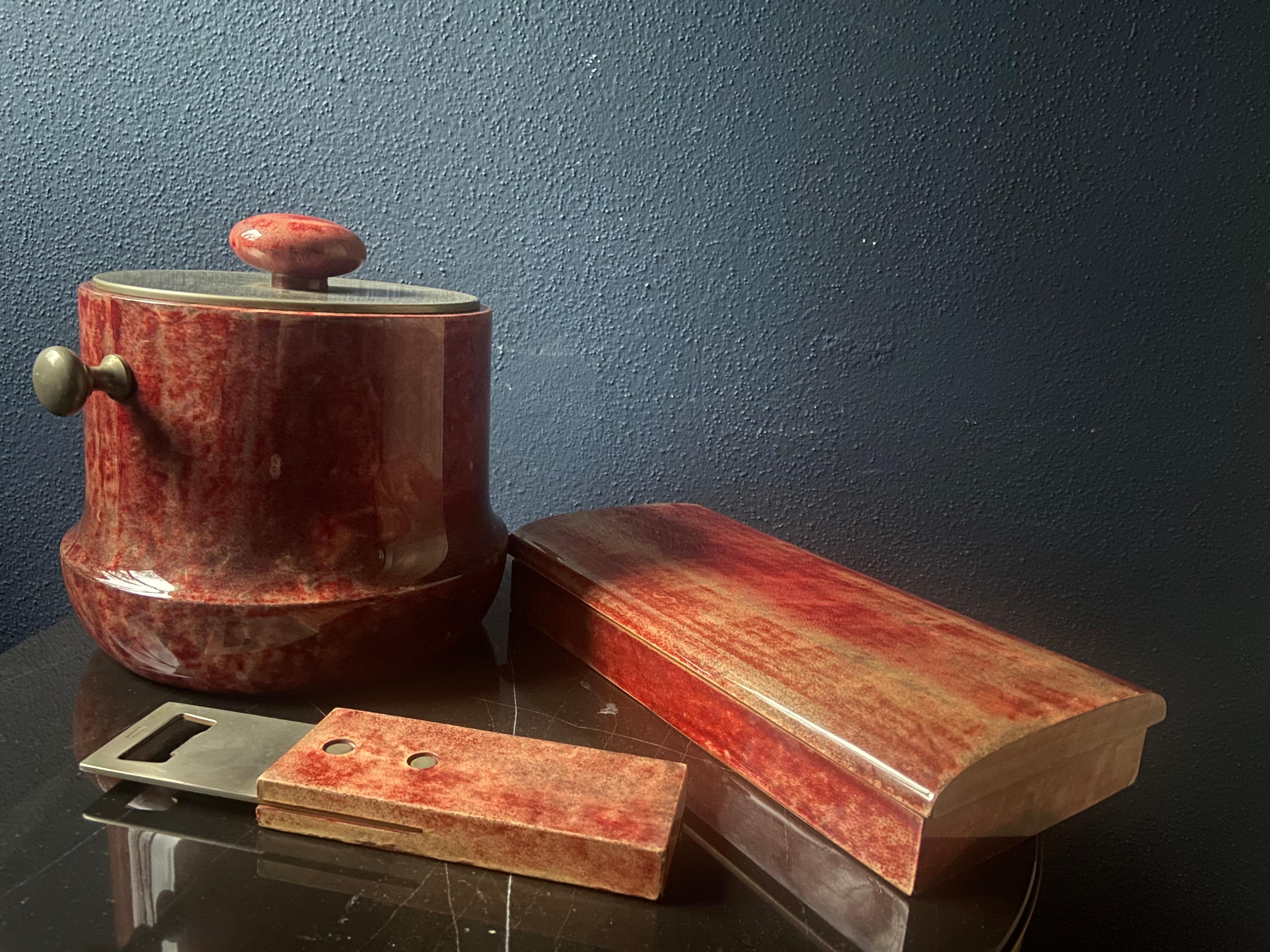 This eclectic trio of Aldo Tura bar accessories consisting of an ice cooler, a large bottle opener and a decorative box oozes with Italian Mid-Century Modern charm.

In typical Aldo Tura fashion the accessories are covered lacquered goatskin which