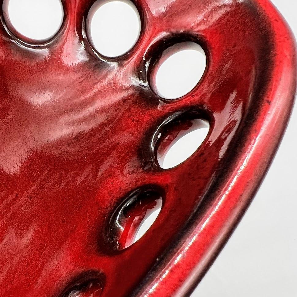 Inspired by organic contemporary design, this pierced oblong bowl is wheel thrown, distorted and hand pierced stoneware with a glossy red glaze that breaks to black along the edges. Small holes are created when the clay is still wet and then each