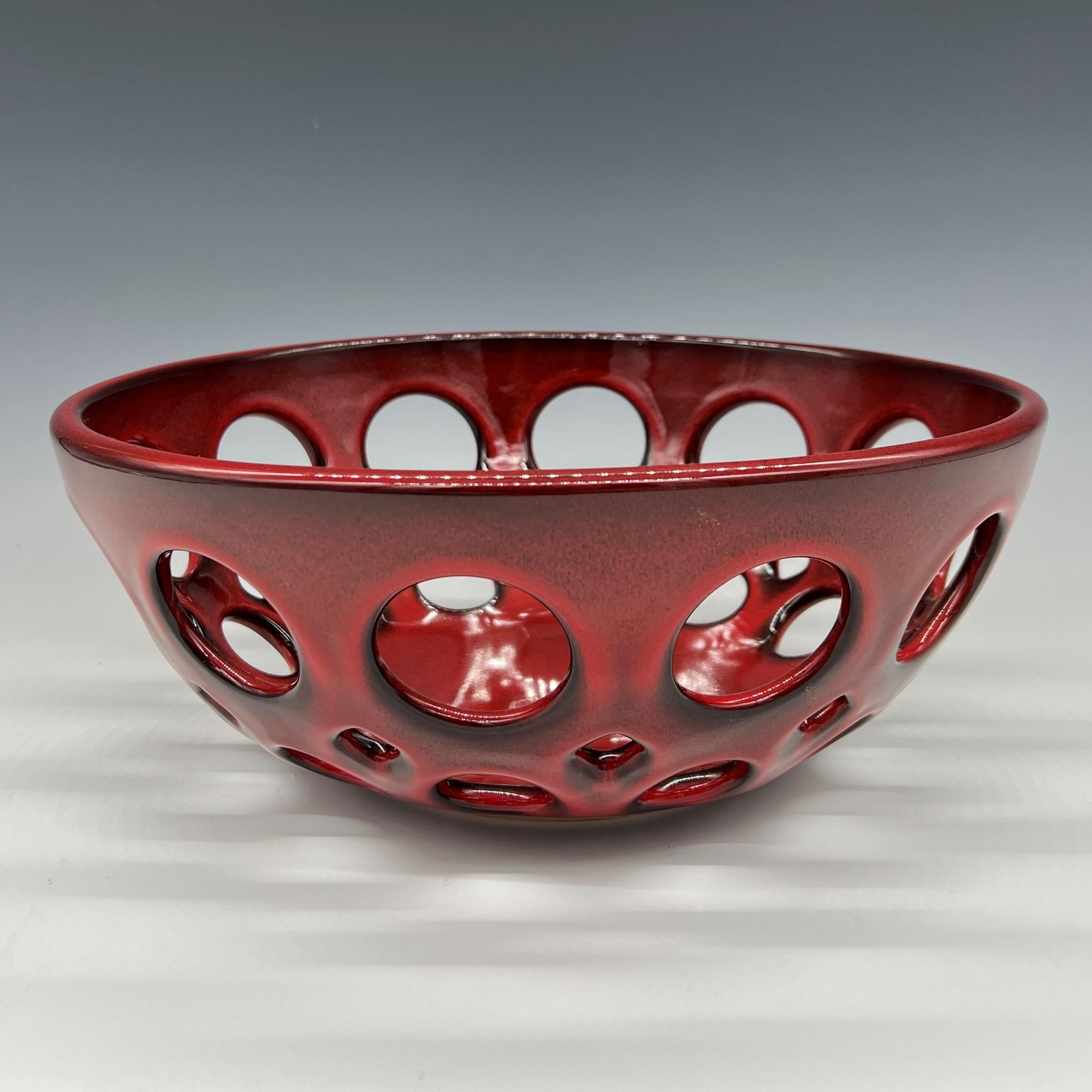 Inspired by Mid-Century Modern design, the pierced collection is wheel thrown and hand pierced stoneware with a glossy red glaze that breaks to black along the edges. Small holes are created when the clay is still wet and then each hole is