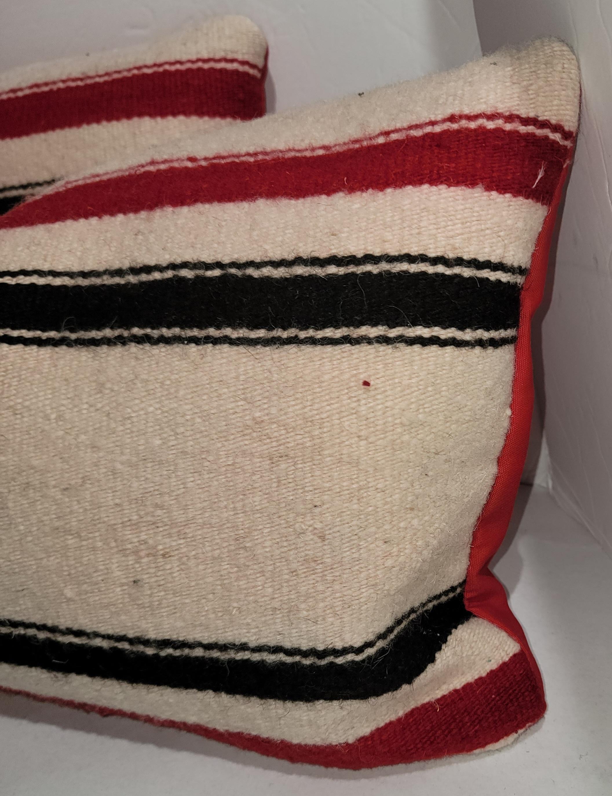 Clean wool red and black striped saddle blanket pillows with a clean white wool background. There is a bright red linen backing used for this pair of pillows.  Down and feather inserts for each.