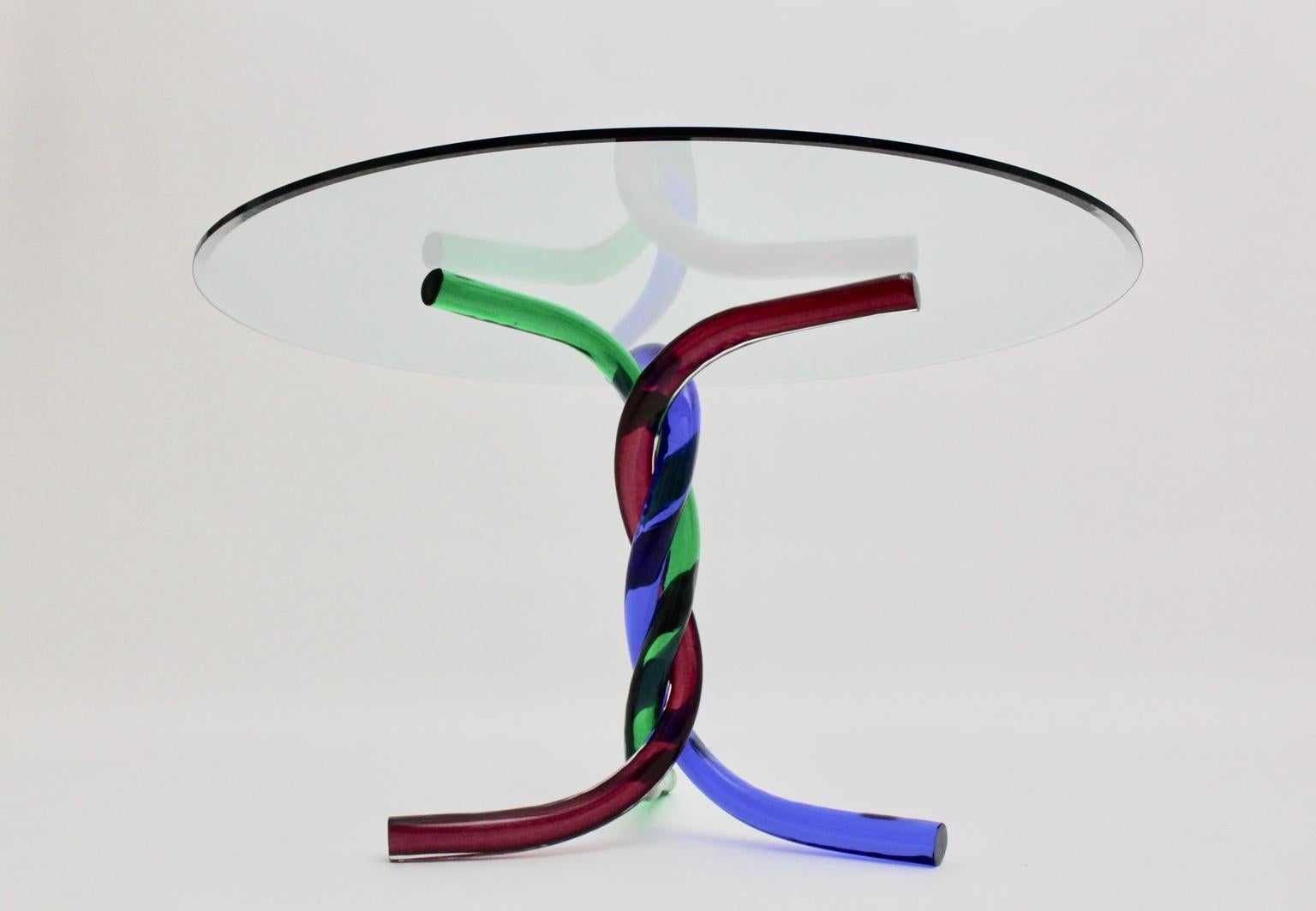 Mid Century Modern vintage glass dining table or center table, which was designed and manufactured in Murano,  Italy 1970. The rare dining table features a colorful base of three curved glass elements in the colors red, blue and green with a round