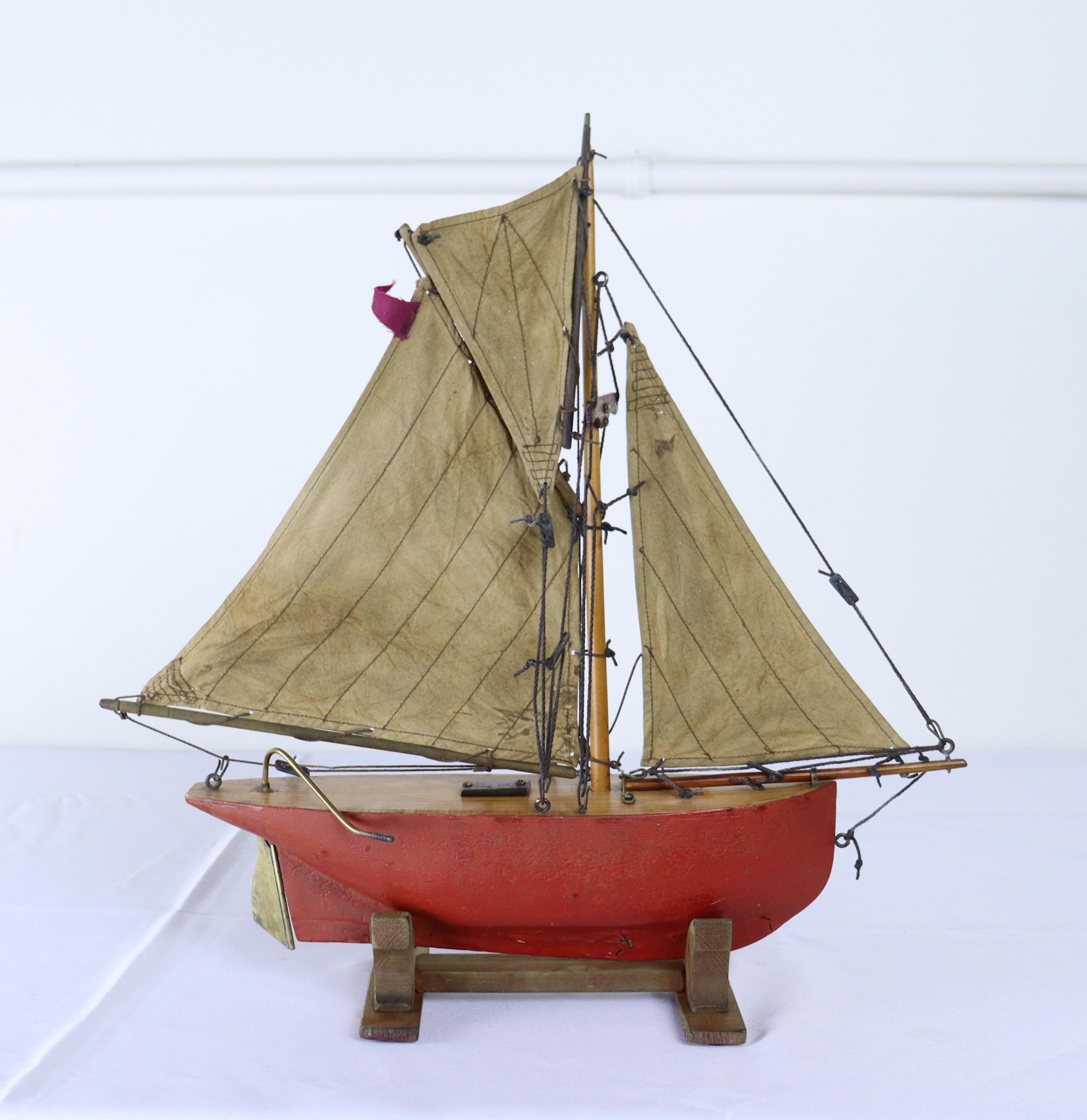 A charming vintage model yacht with sails made from old sail cloth and original brass accents. Stand is recent to hold the ship upright and stabile.  Measurements include the stand.