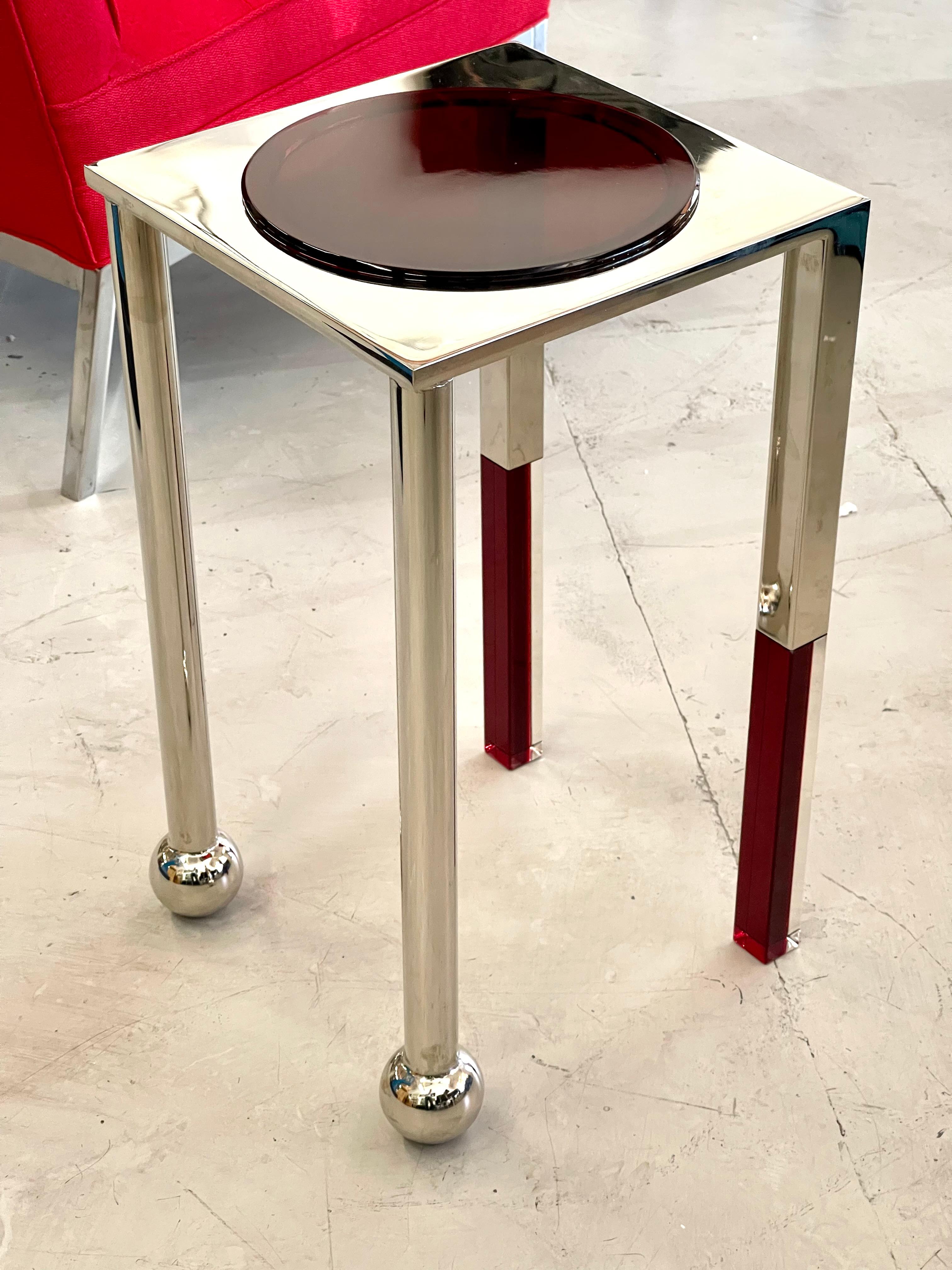 A sculptural table in red and clear acrylic by Charles Hollis Jones. It is one of two new designs by the noted designer. Please see the companion in blue and clear. These has nickel plated finishes and are 21 inches tall and 12 inches square. In