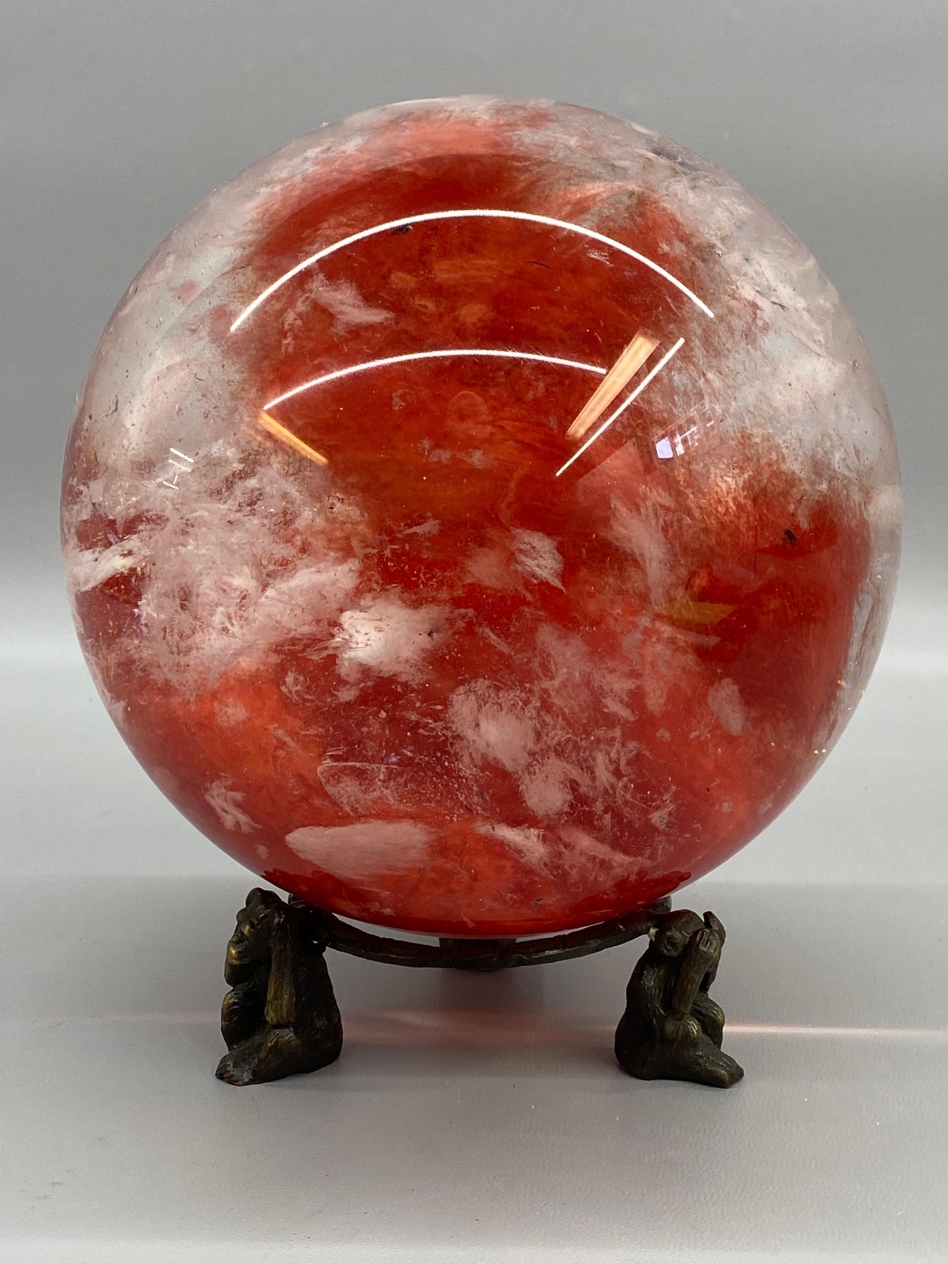 Eine hervorragende und schöne Kristallkugel mit Ständer. Das Glas ist eine feine Mischung aus roten und weißen Wolken mit einigen natürlichen Einschlüssen, die diesem Objekt eine geheimnisvolle Note verleihen. Der dreibeinige Ständer ist aus Bronze