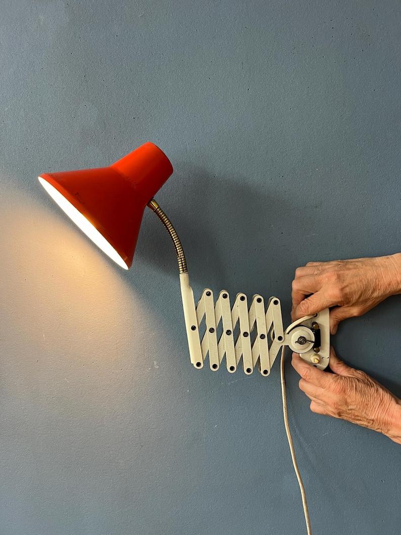 Hala Zeist scissor wall lamp made out of metal with red and white lacquer. The piece can turn left, right, up and down from the wall bracket position. The length of the lamp can easily adjusted with the scissor mechanism. The lamp requires an E27/26