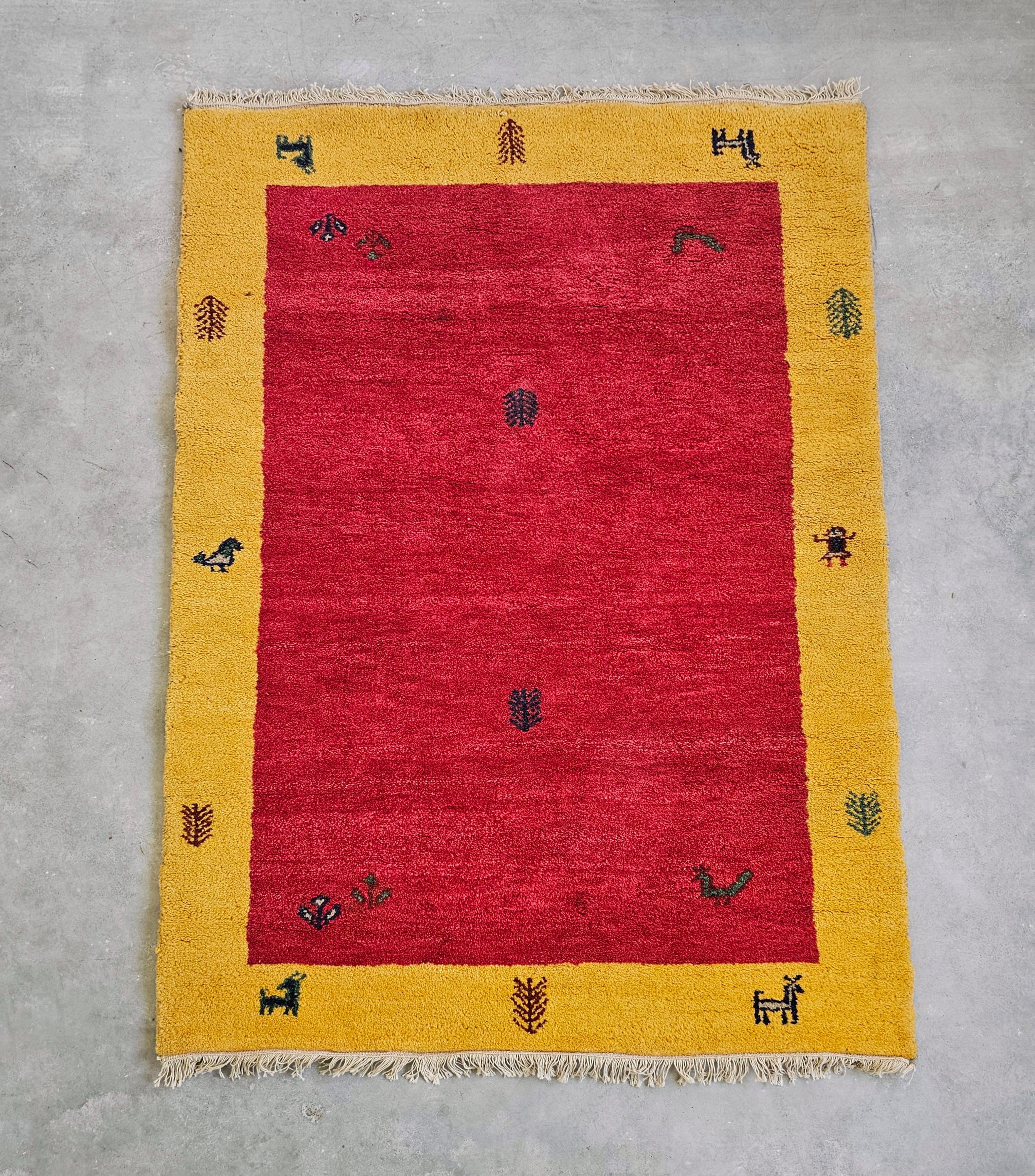In diesem Angebot finden Sie einen roten und gelben Gabbeh-Teppich mit einer sehr begrenzten Anzahl von charakteristischen abstrakten Mustern, die an Tiere und Menschen erinnern. Sein Design vereint zwei Ästhetiken, die nicht oft kombiniert werden -