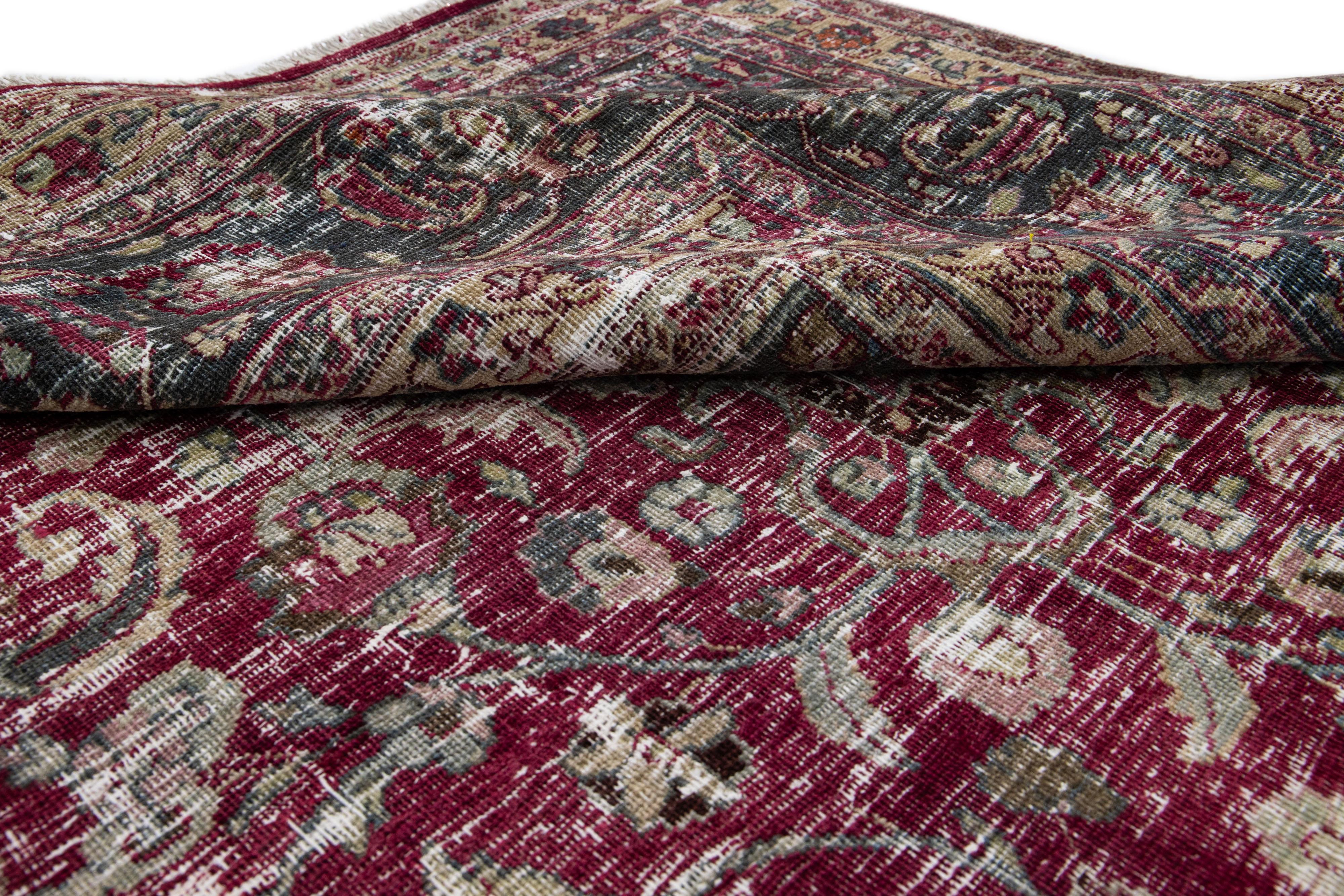 Magnifique tapis ancien en laine de Mashad, noué à la main. Ce tapis présente un champ rouge avec des accents verts et feu. Ce tapis présente un motif traditionnel en médaillon au centre.

Ce tapis mesure 11' 3