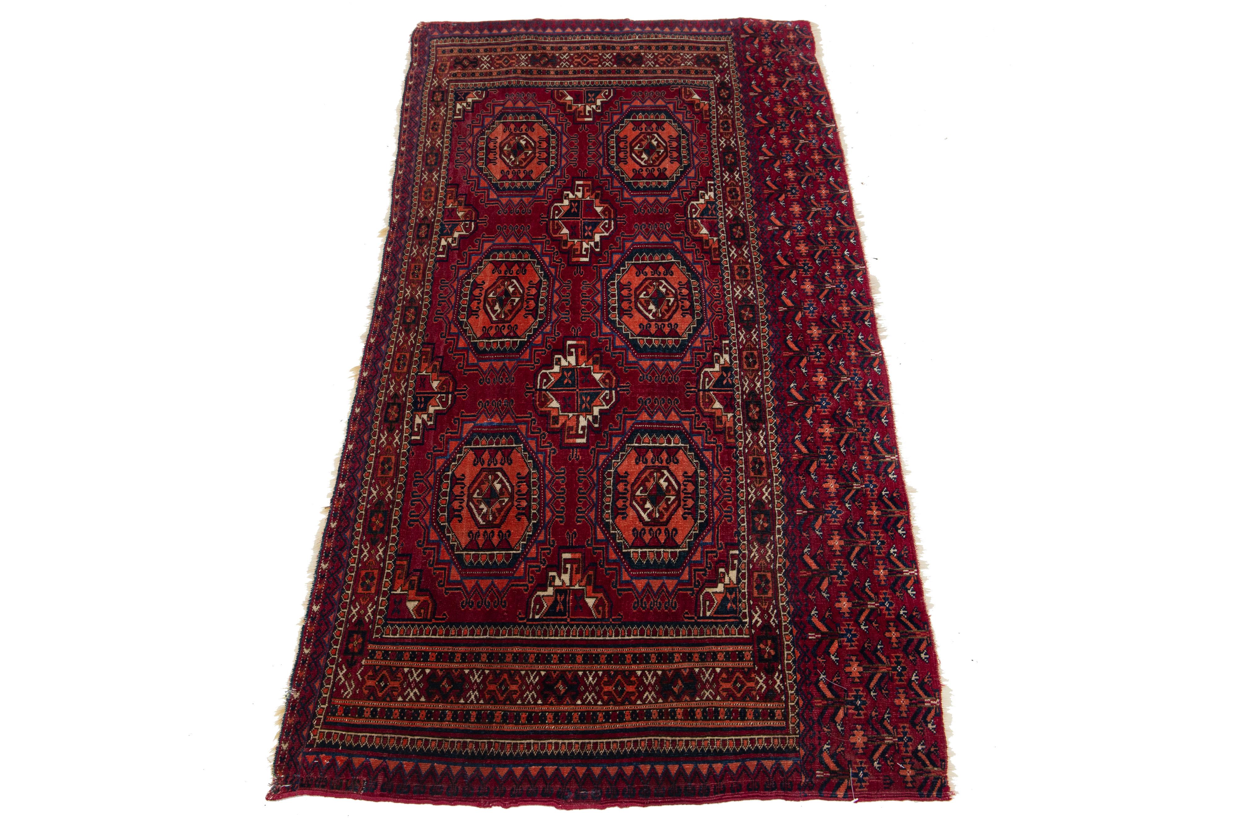 Ce tapis vintage en laine nouée à la main au Turkménistan présente un champ de couleur rouge, des accents bleu marine, beige et orange, et des franges dans un motif géométrique complexe.

Ce tapis mesure 2'6