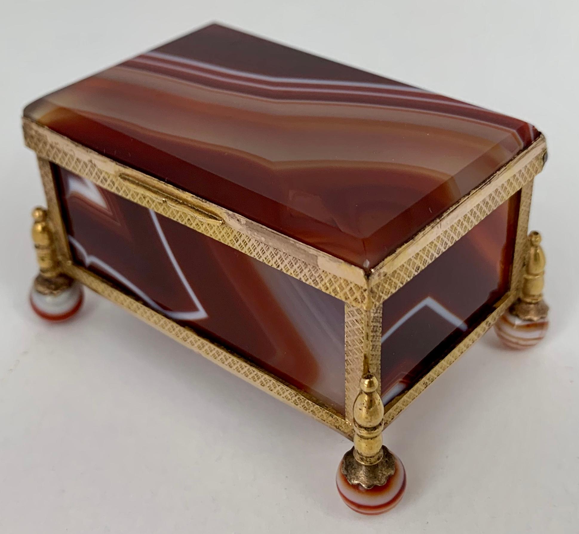 Stunning red banded hinged agate box with gilt brass frame. The pieces of stone are beveled on the interior while the petit box rests on ball feet.  Perfect for jewelry, stamps or whatever you desire.  Hand polished in our workshop. (19th