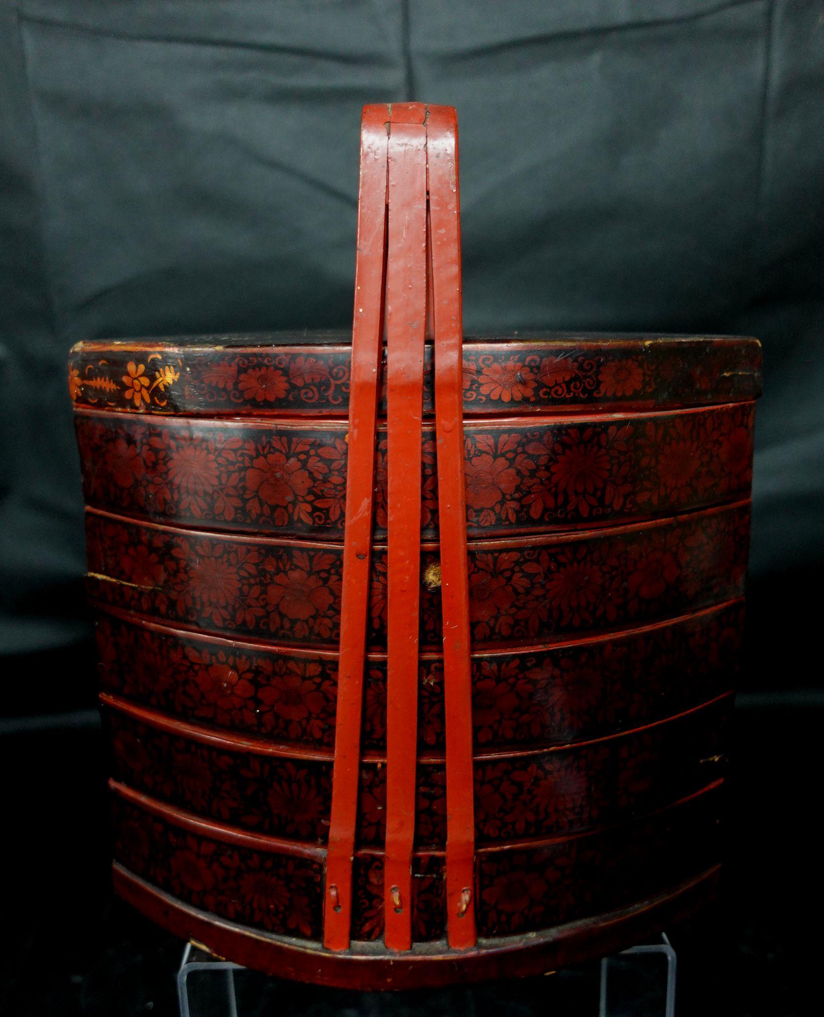 Red/Black-lacquered Fan-shape Five-case Lunch Box, China, 19th century, with three bamboo splint handles converging to form a broad strap handle over the top, decorated with chrysanthemum flower heads.