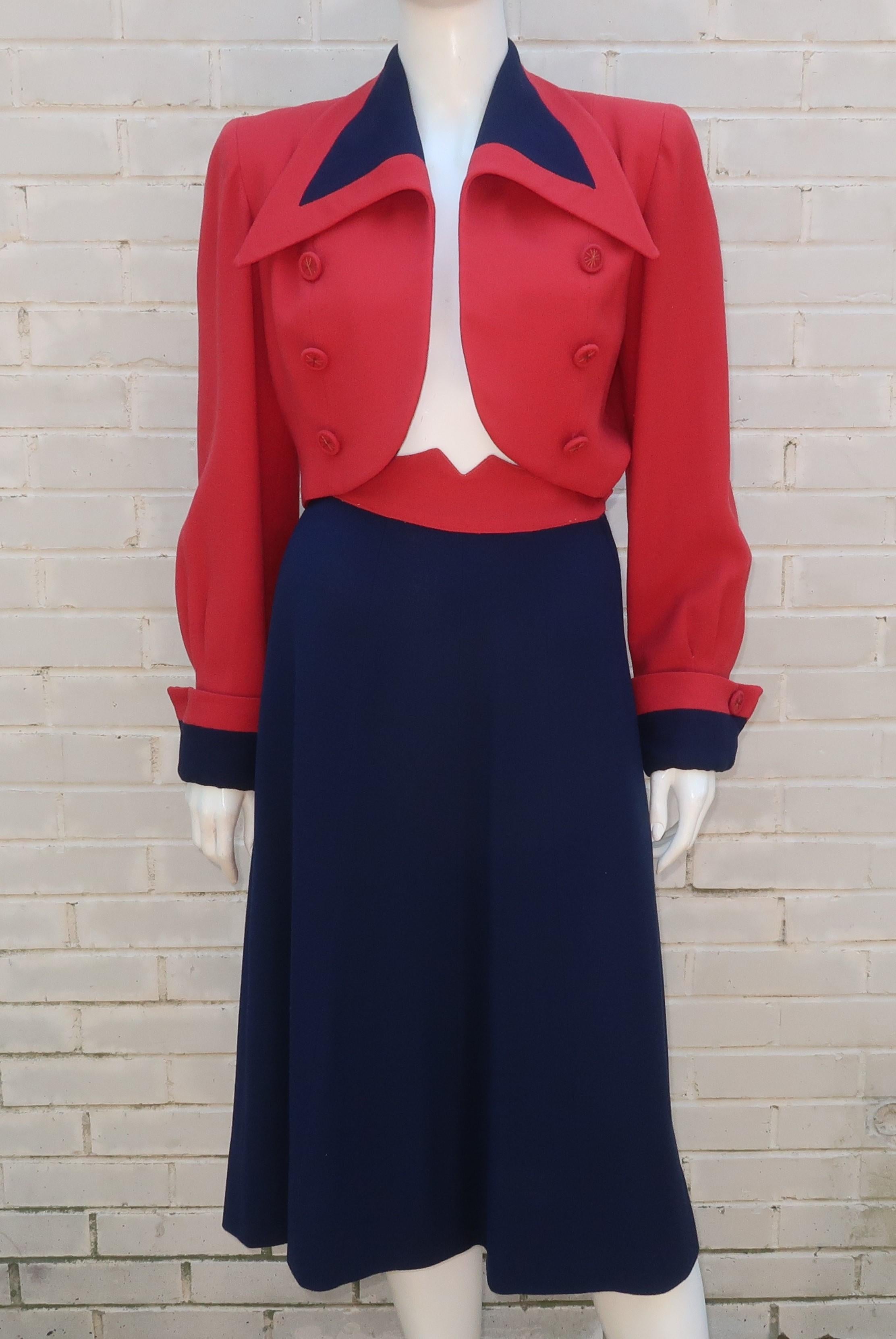 patriotischer Anzug im Stil der 1940er Jahre aus rotem und blauem Krepp mit abgeschnittener Jacke.  Die Jacke ist eine stilisierte Version des Military-Looks mit spitzem, breitem Kragen, überschnittenen Schultern, umgeschlagenen Manschetten und