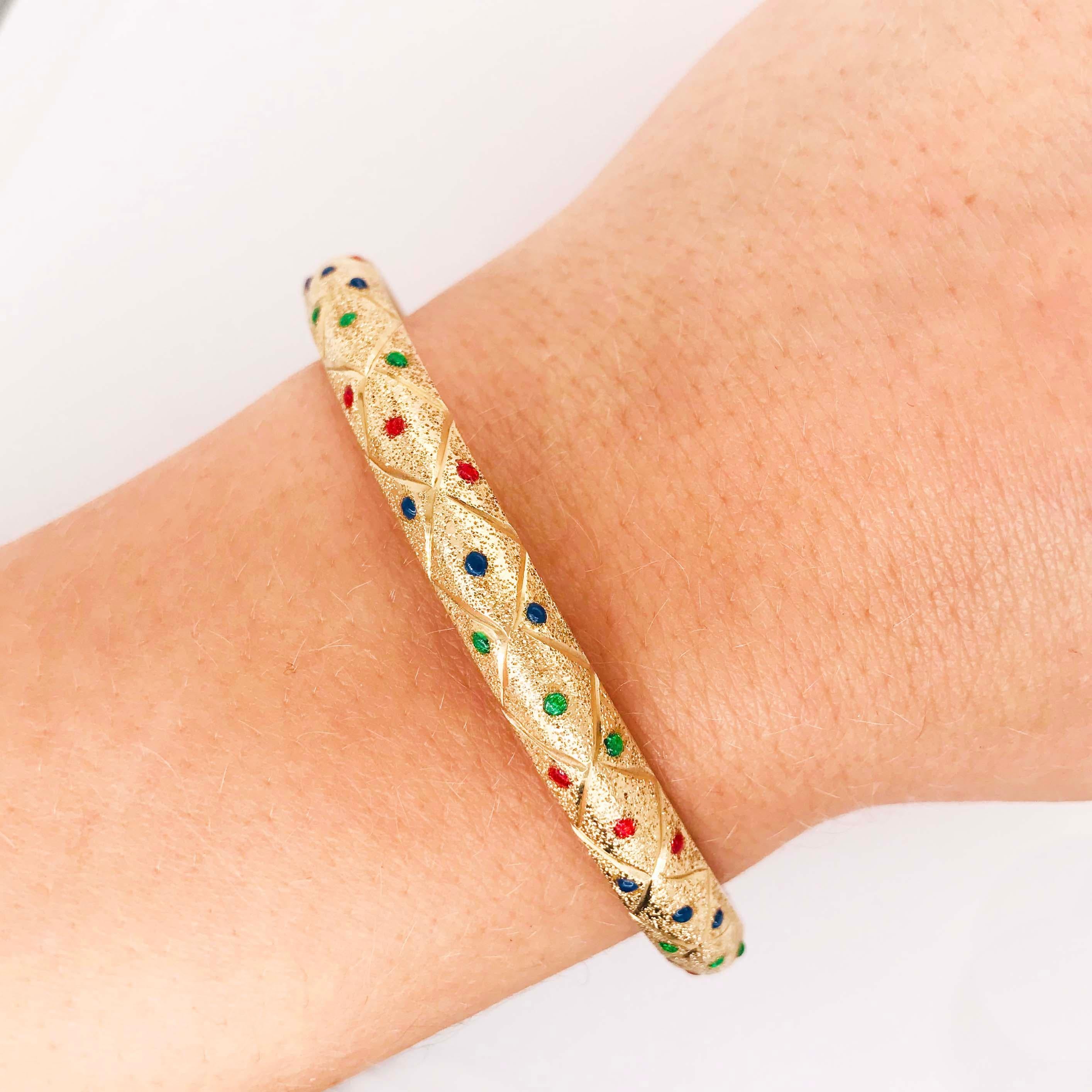 This gorgeous gold bangle bracelet is a custom fine jewelry piece. The 14k handmade gold bangle has a one of a kind design! On the bangle there is a fun, bold pattern of red, blue and green enamel dots that are in an angled pattern. The colors are